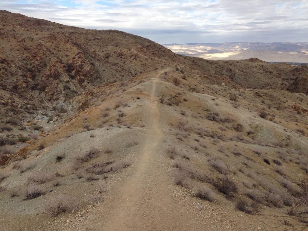 A dirt trail winds up a barren, rocky hill under an overcast sky.