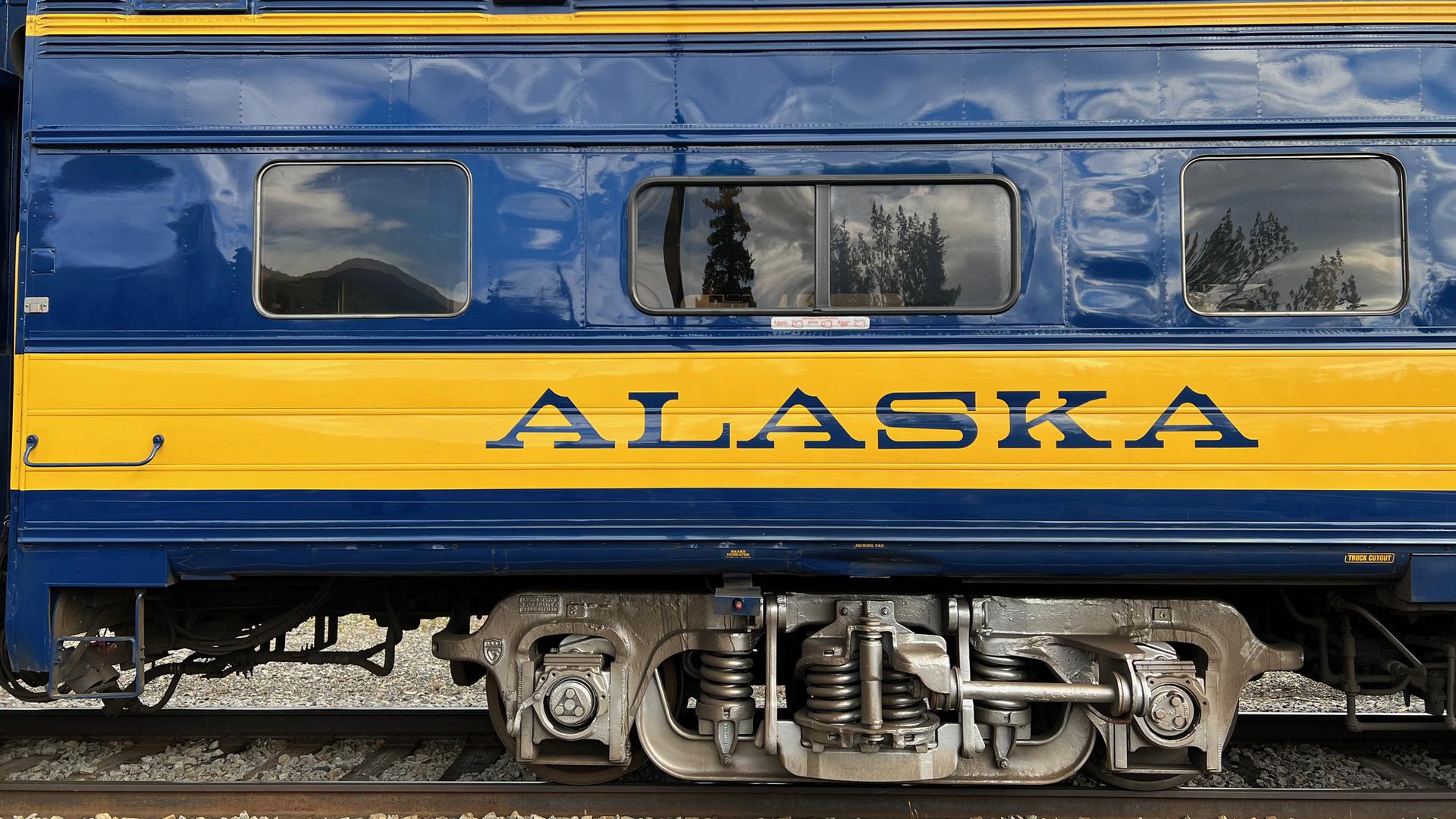 Blue and yellow train car with "ALASKA" text, showing wheels and windows.
