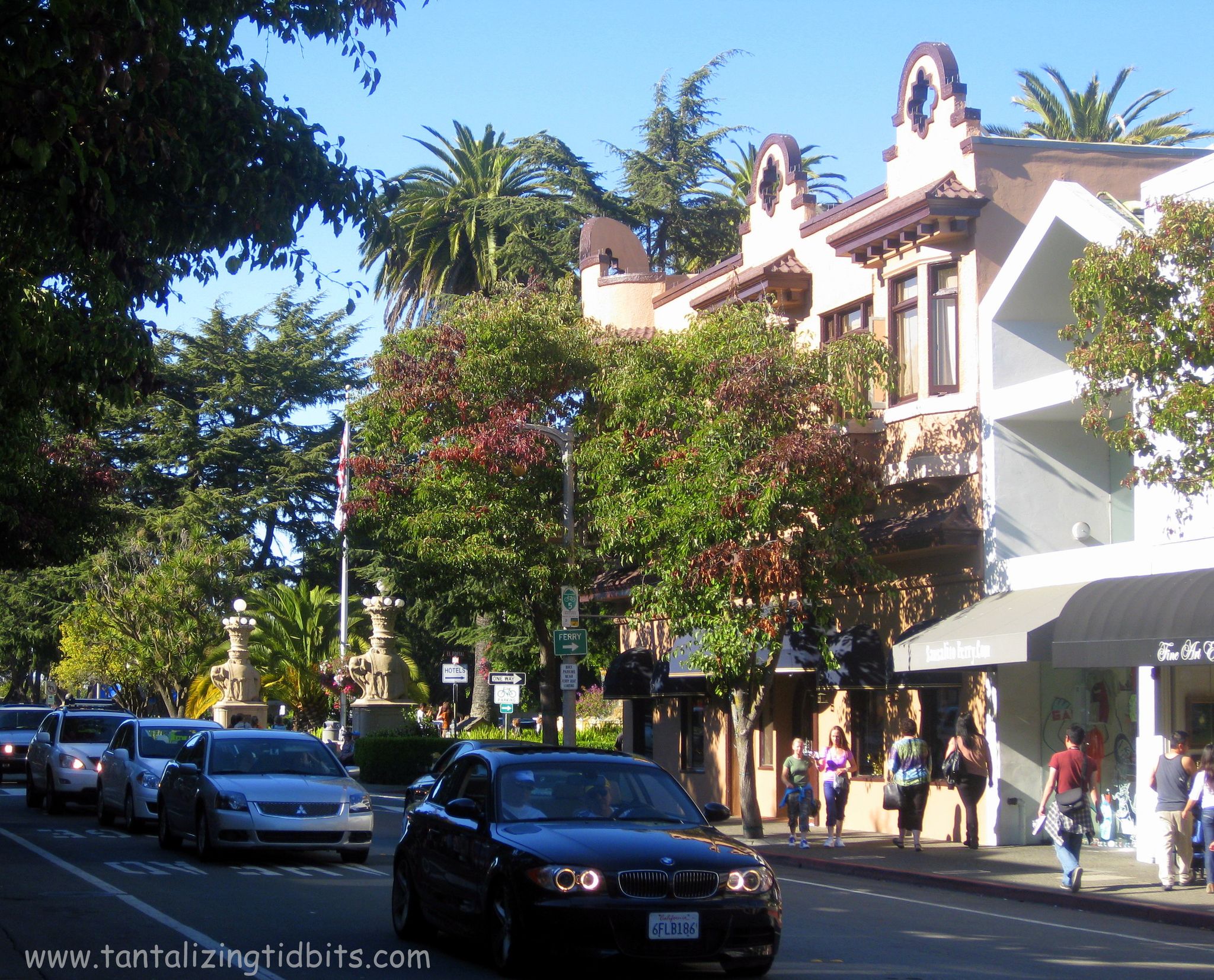A sunny street scene with cars, pedestrians, and ornate buildings under palm trees. - Sausalito Yacht Harbor – Downtown Sausalito loop from Sausalito