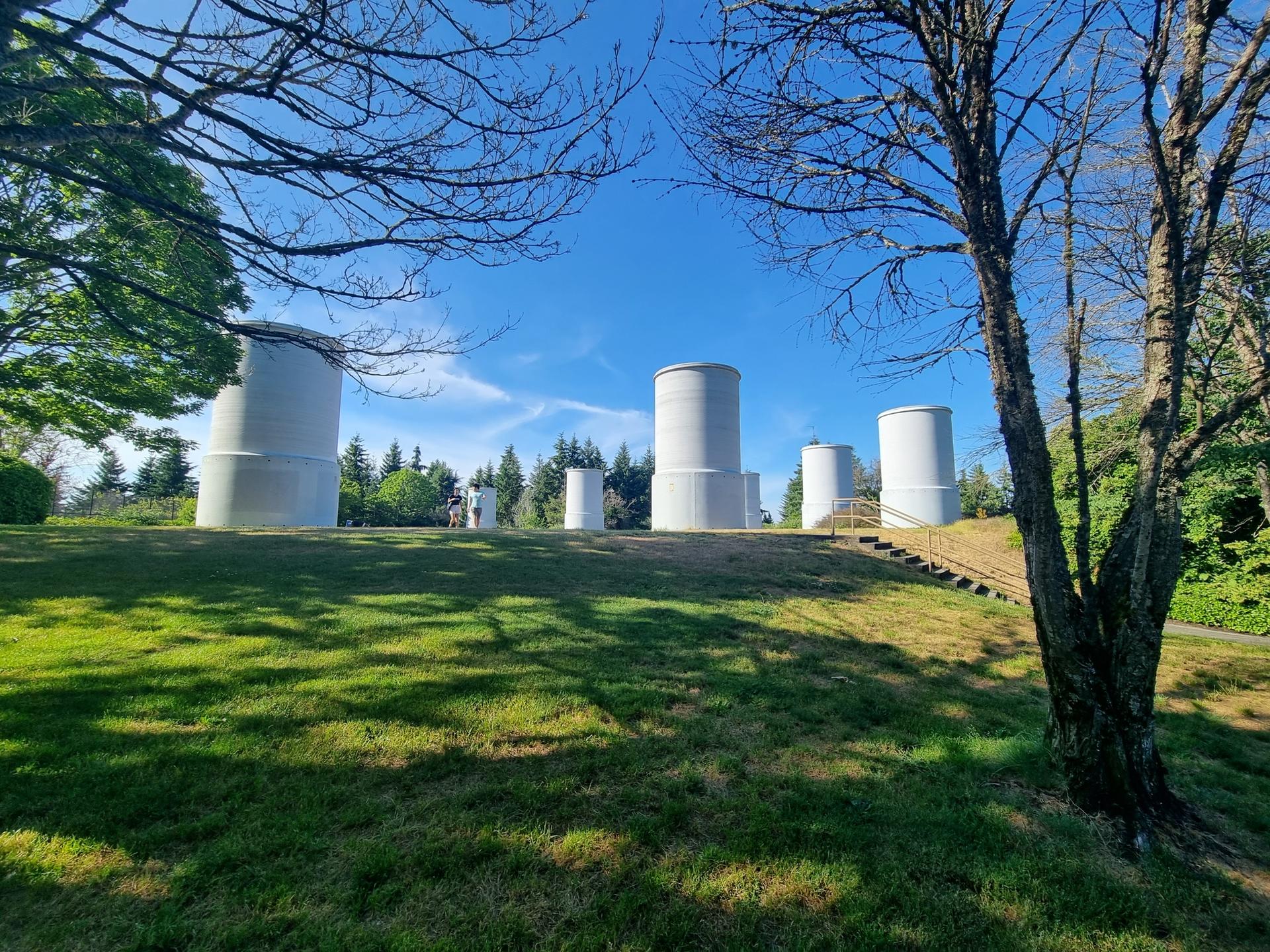 Several large white cylindrical structures on a grassy hill under a clear blue sky.