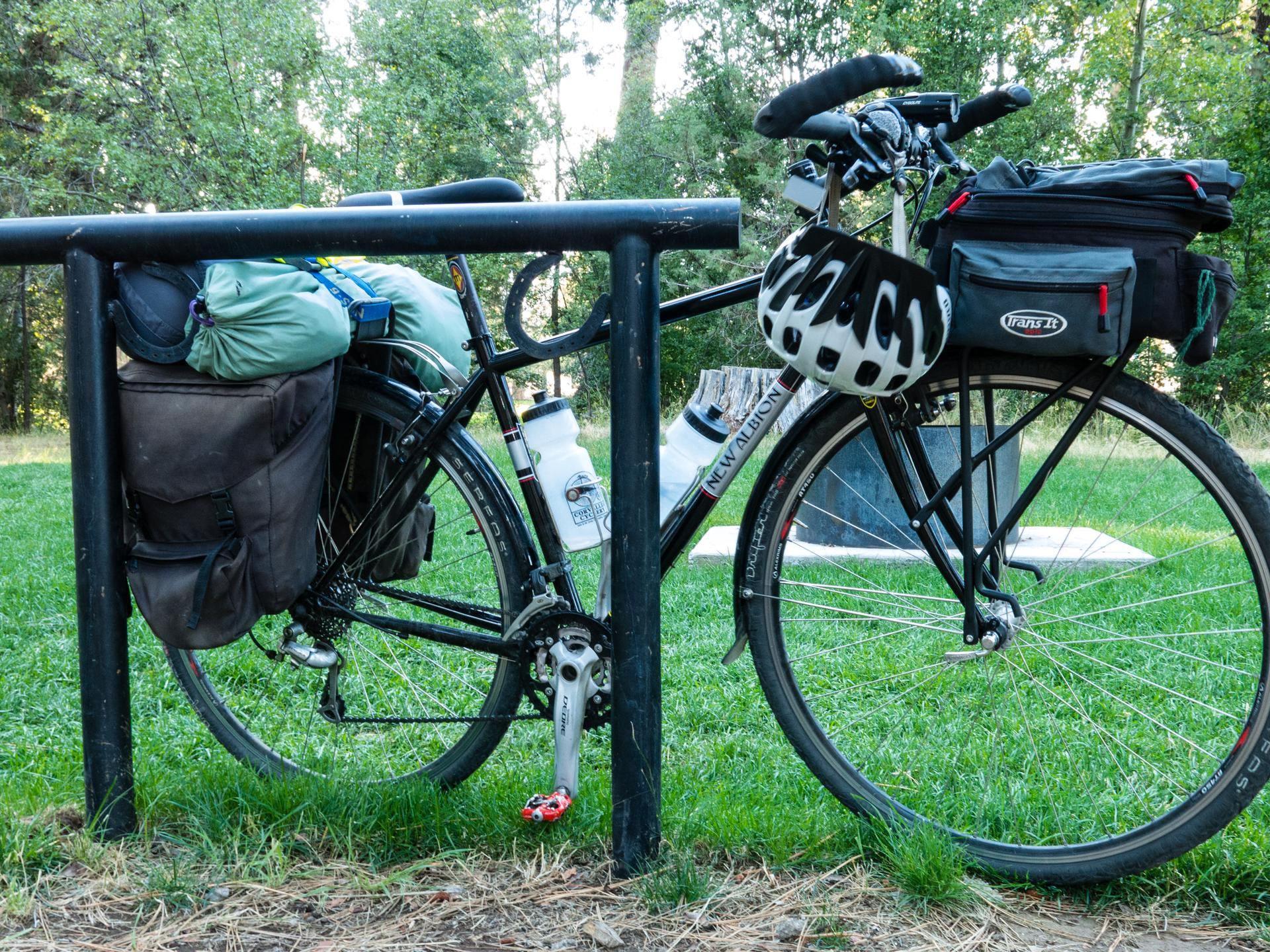 A touring bicycle with panniers and a helmet parked on a grassy area.