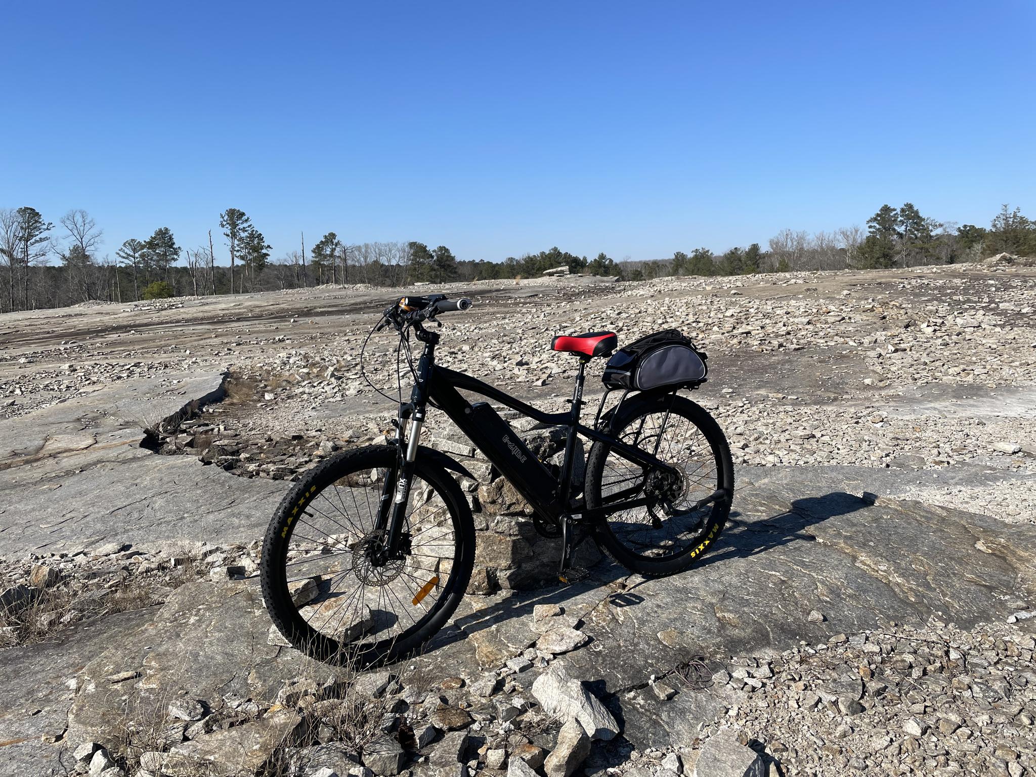 A black bicycle with a red seat rests on a rocky, barren landscape under clear skies.