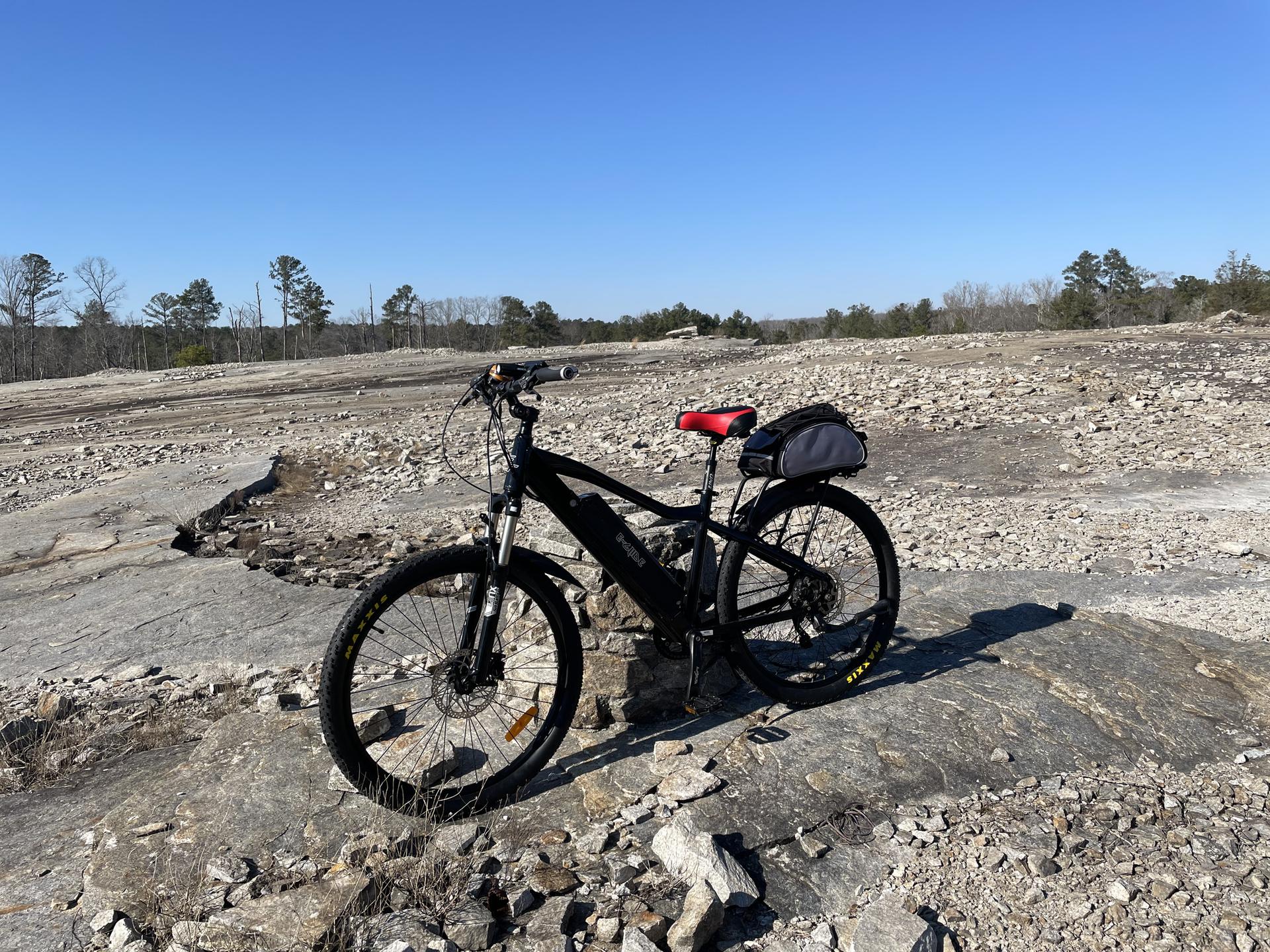 A black bicycle with a red seat rests on a rocky, barren landscape under clear skies.