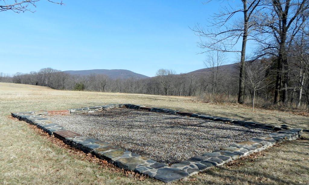 A stone foundation outline sits in a dry field with distant mountains.