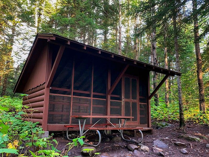 Small wooden cabin with a screened porch and picnic table in a forest.