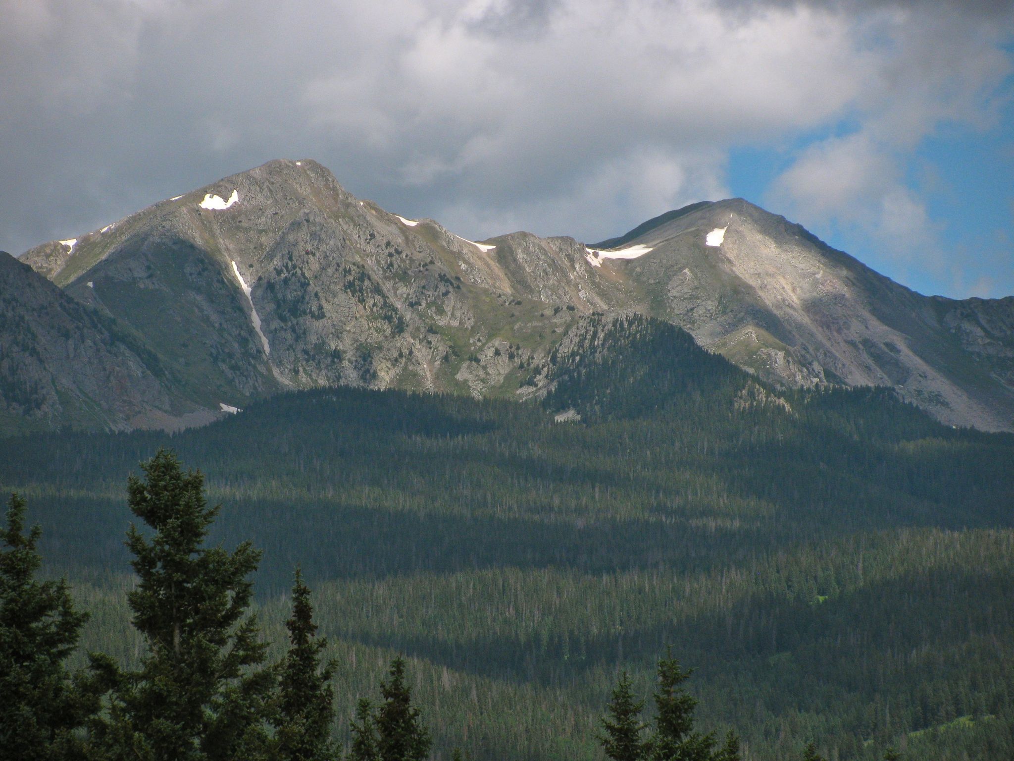 Rocky mountains with snow patches above a dense evergreen forest under cloudy sky. - Hamilton Mesa Loop
