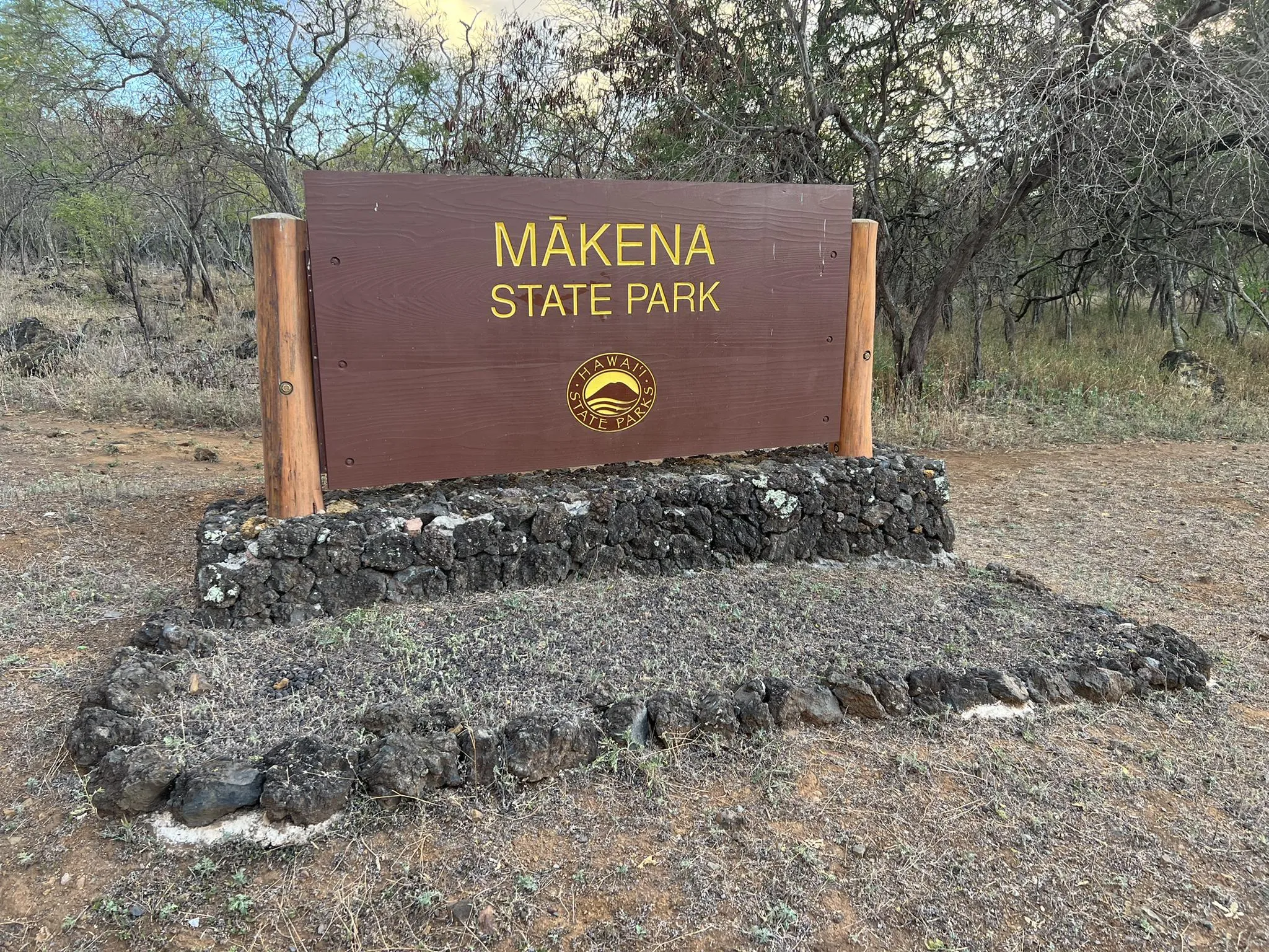 A brown wooden park sign on a rocky base in a dry, natural area. - Wailea Beach – Mākena State Park loop from Wailea