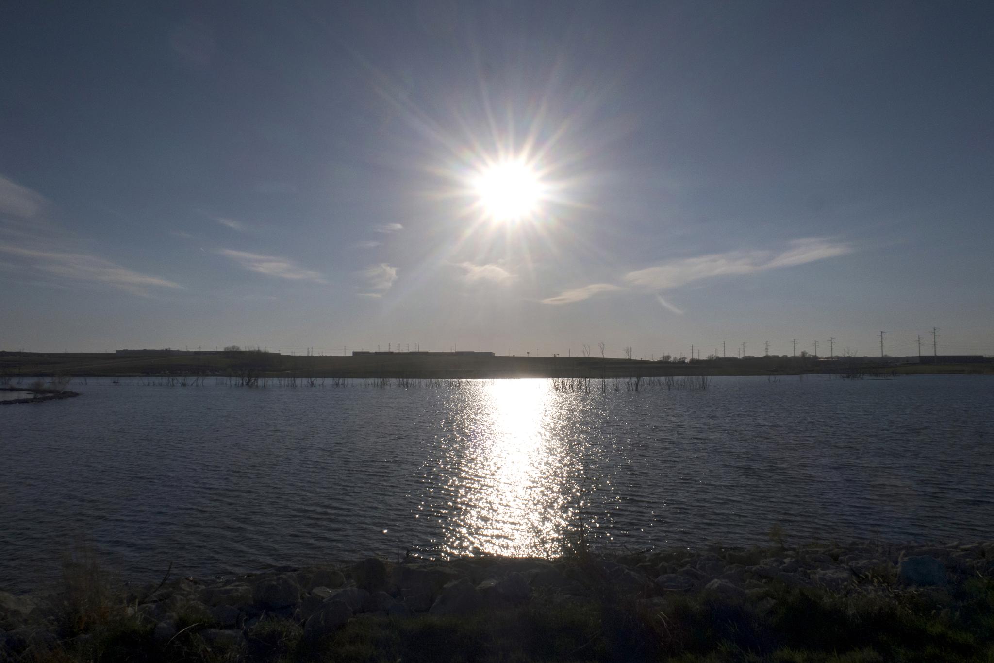 Bright sun shines over a wide body of water, reflecting on the surface.