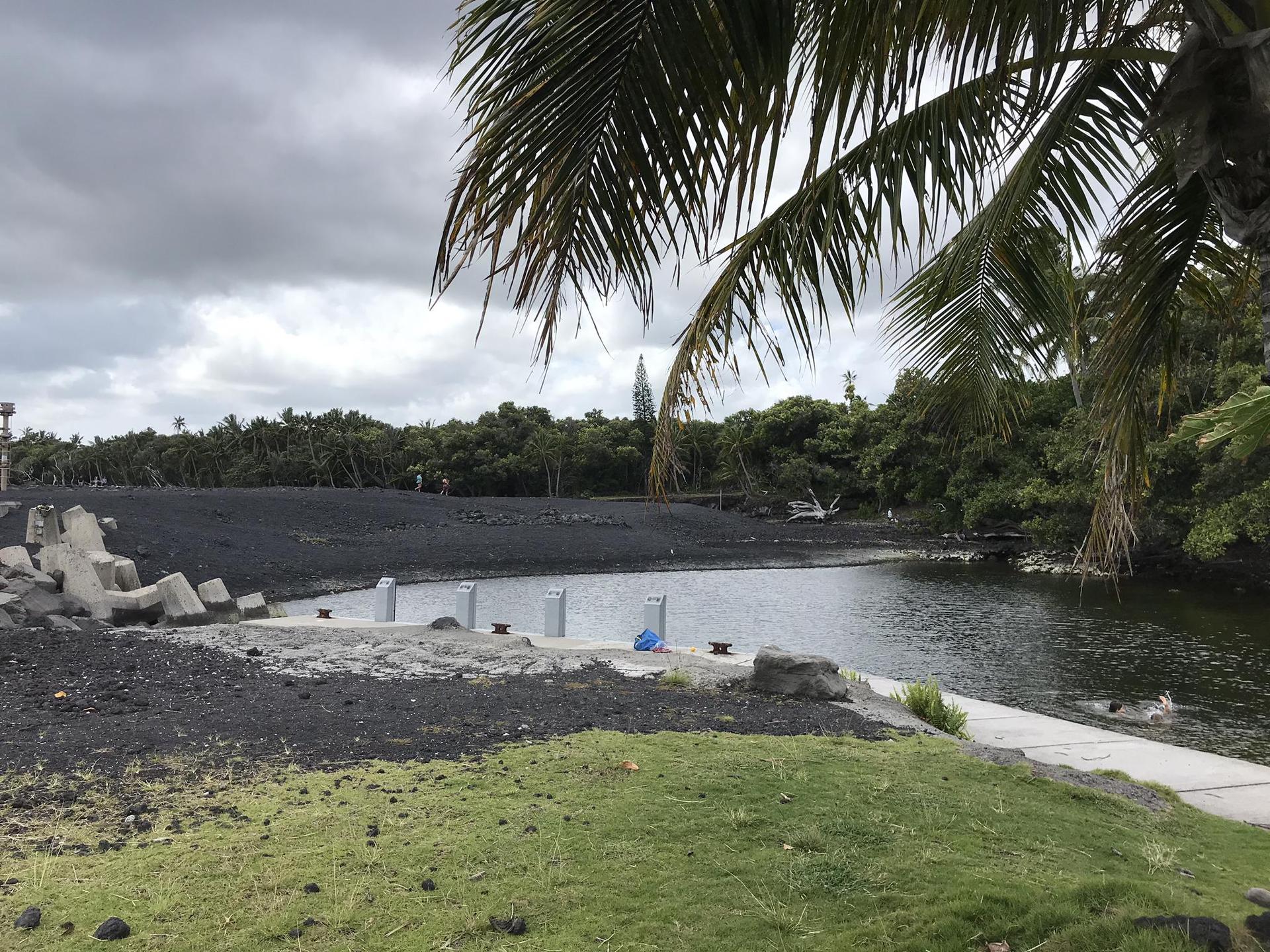 Overcast view of a calm cove with black sand and palm trees.