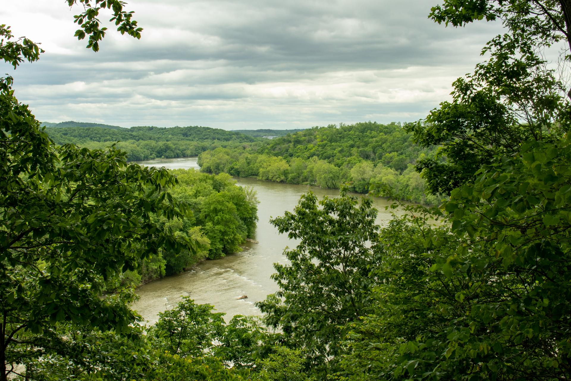 A winding river flows through dense green forests under a cloudy sky.