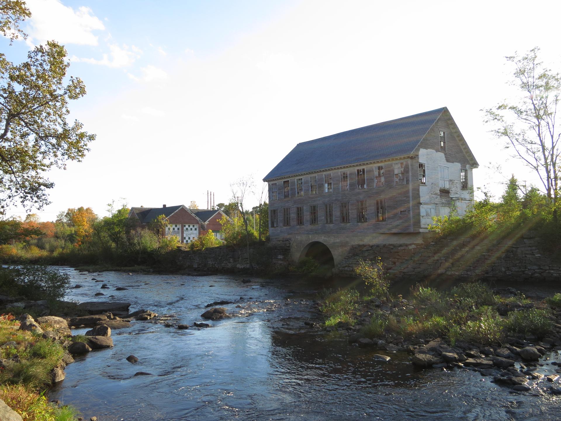 Sunny view of an old mill building beside a flowing, rocky river.
