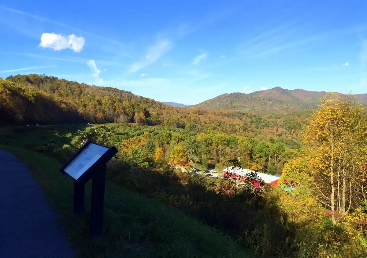 Informational sign overlooking a valley with autumn trees and distant mountains under a blue sky.