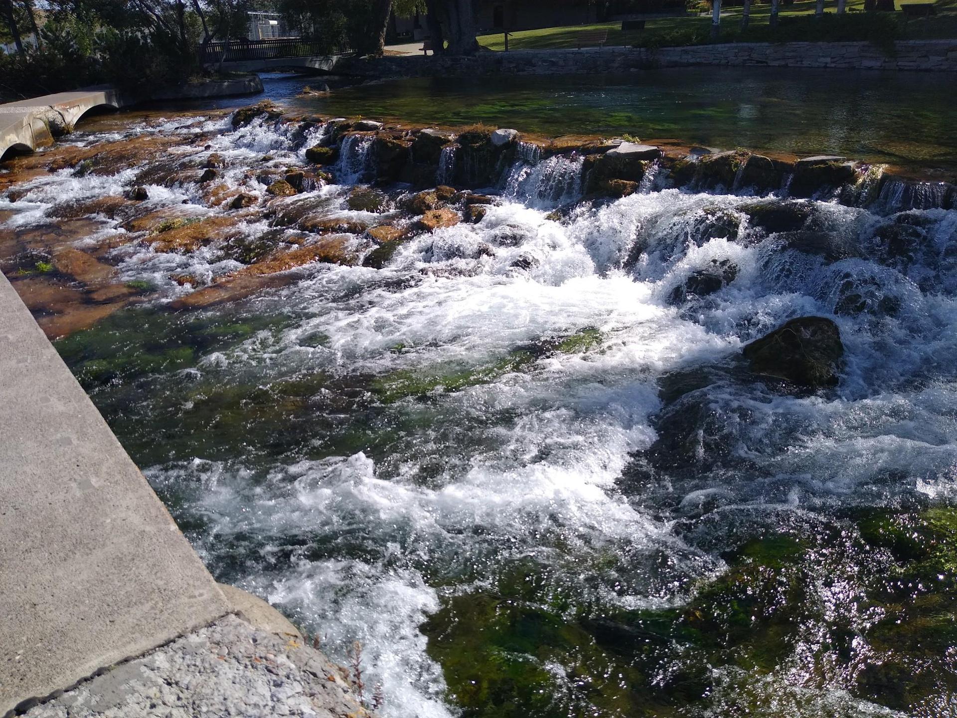 Rushing water cascades over rocks in a shallow, sunlit river.