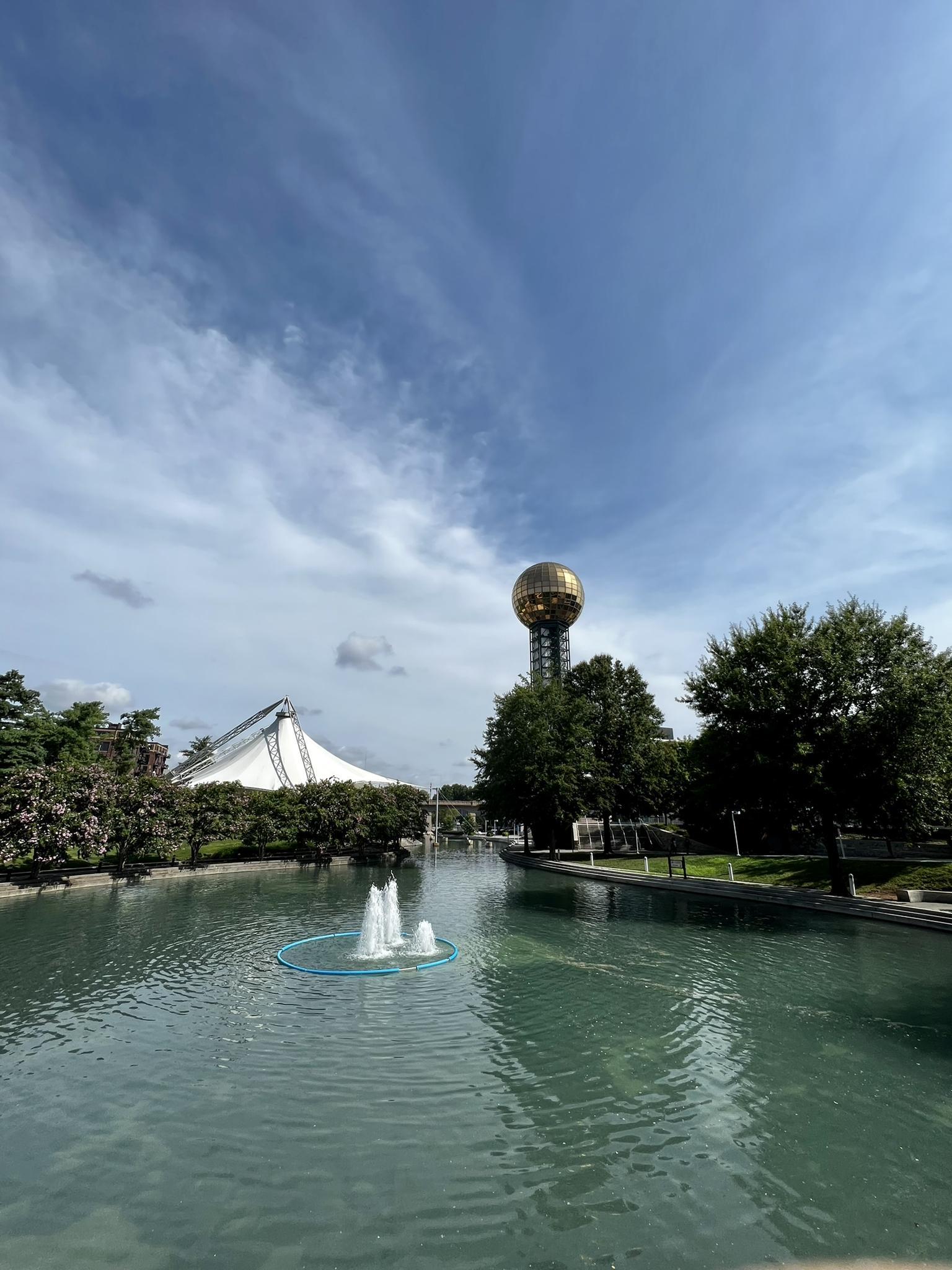 Pond with fountains, a golden sphere tower, and white tent.