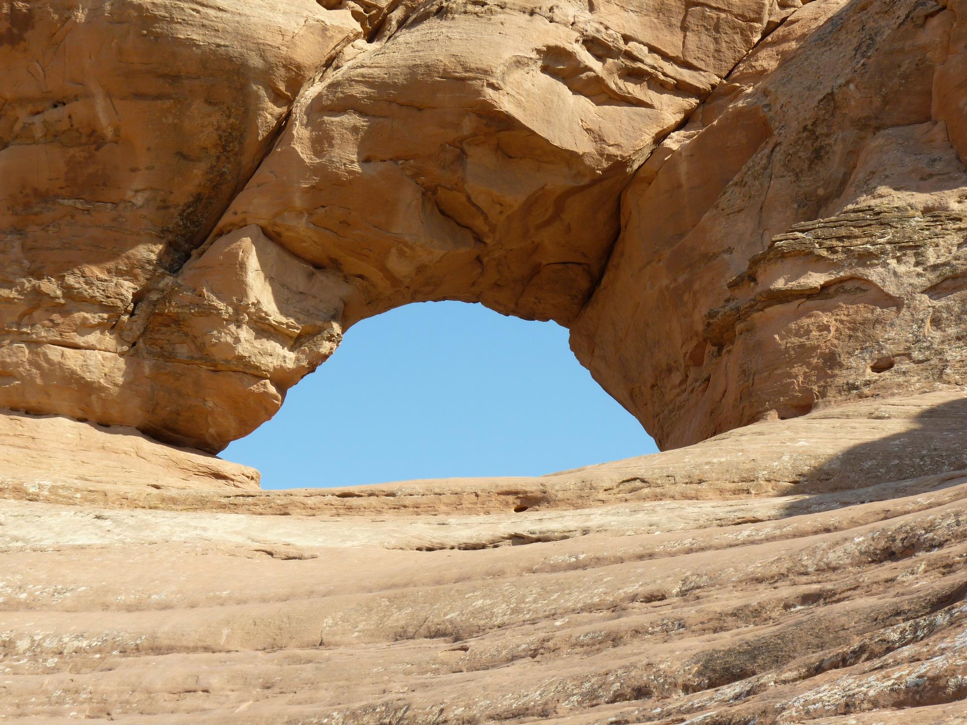 A natural rock arch frames a bright blue sky from a low perspective.