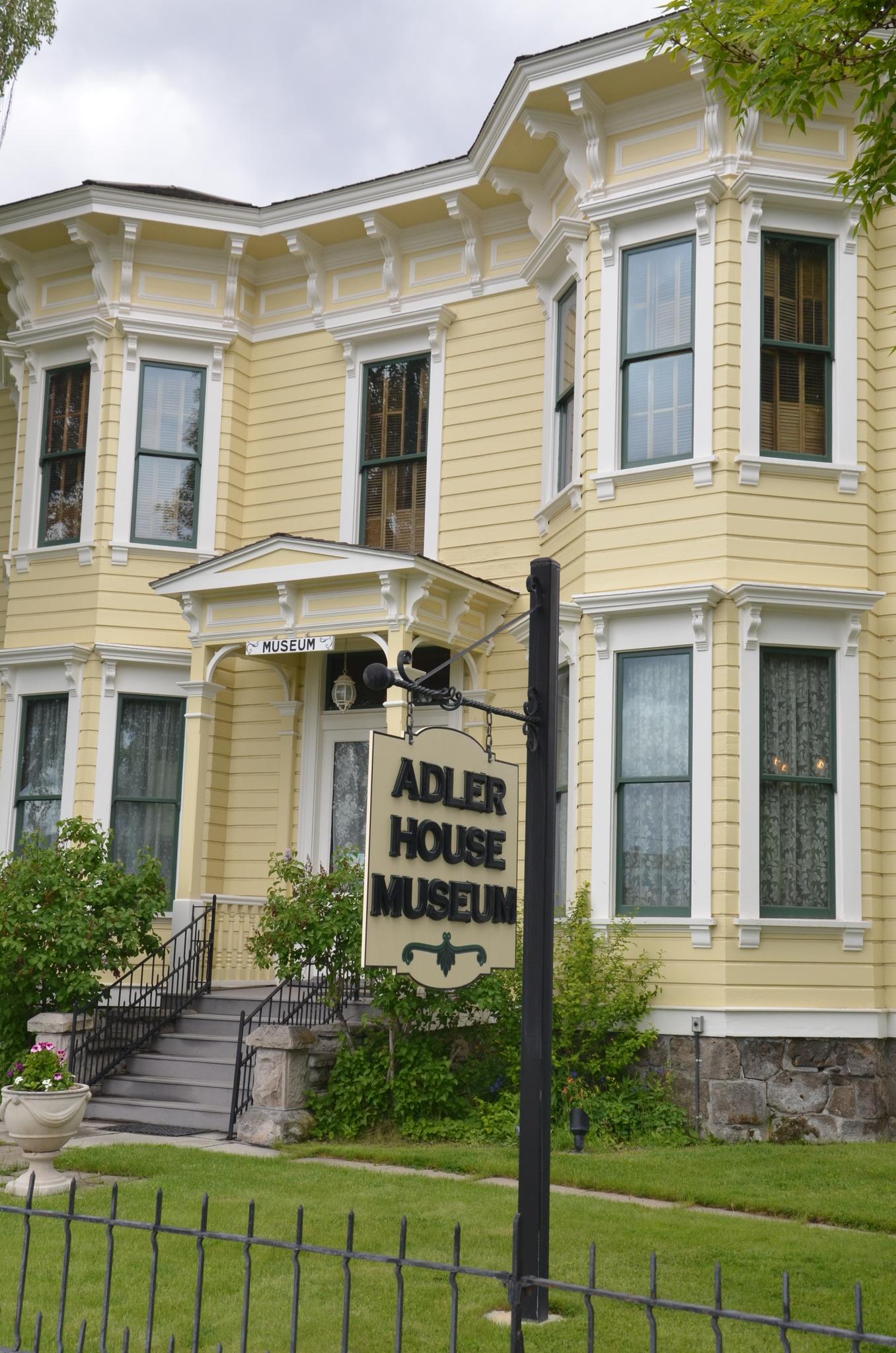 A large yellow Victorian house with a museum sign on a green lawn.