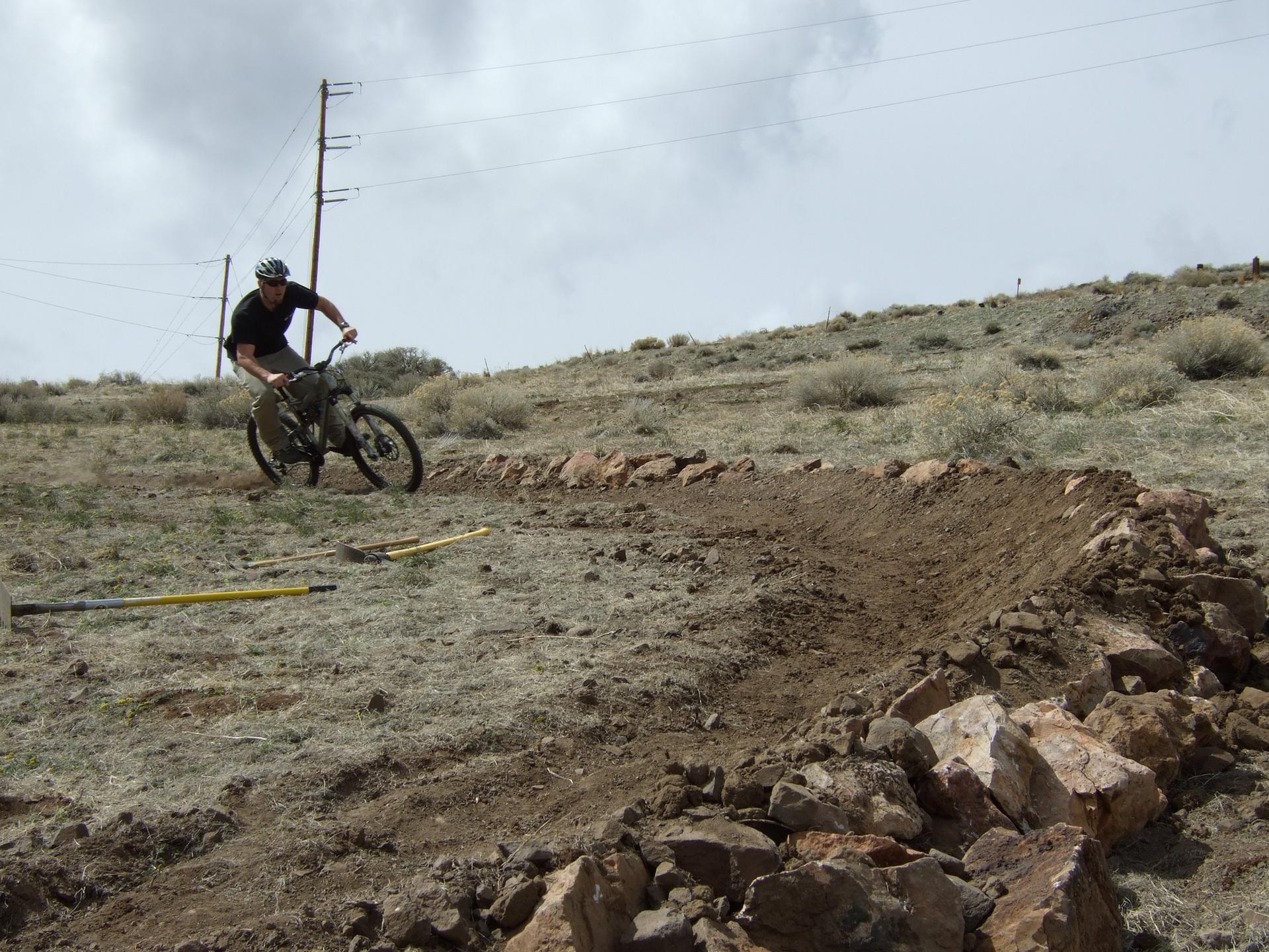 Man mountain biking on a dirt berm under an overcast sky.
