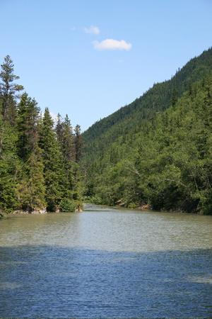 A wide river flows between two steep, tree-covered mountains under a blue sky.