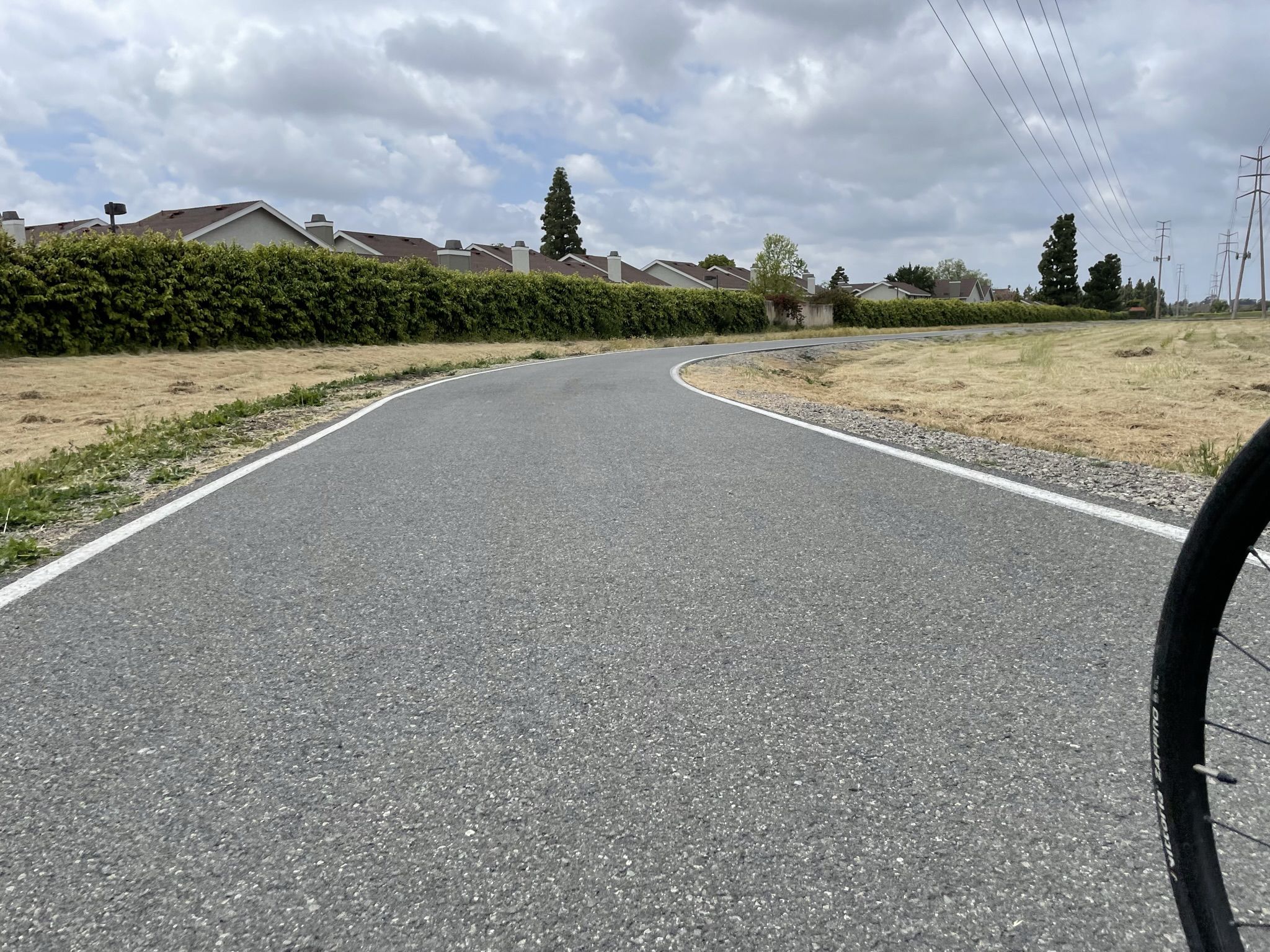 Paved path curving right, with dry grass, houses, and a bicycle wheel. - Santiago Canyon Road loop from Tustin