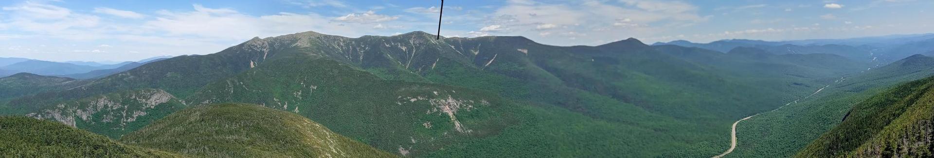 Panoramic view of vast green mountains and valleys under a partly cloudy sky.