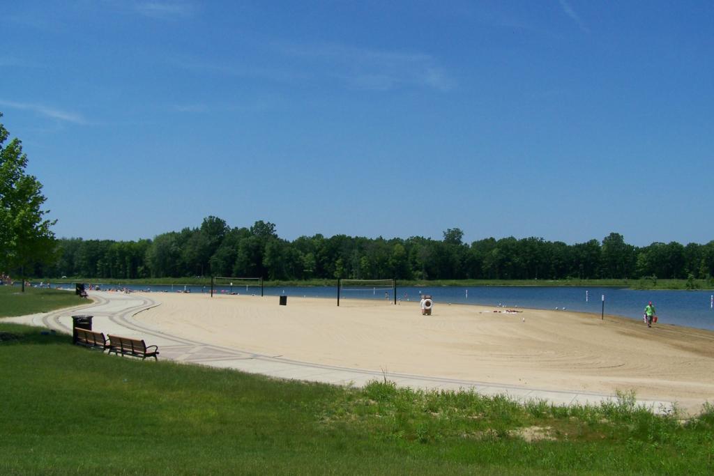 A bright, sunny beach with volleyball nets, water, and distant trees.