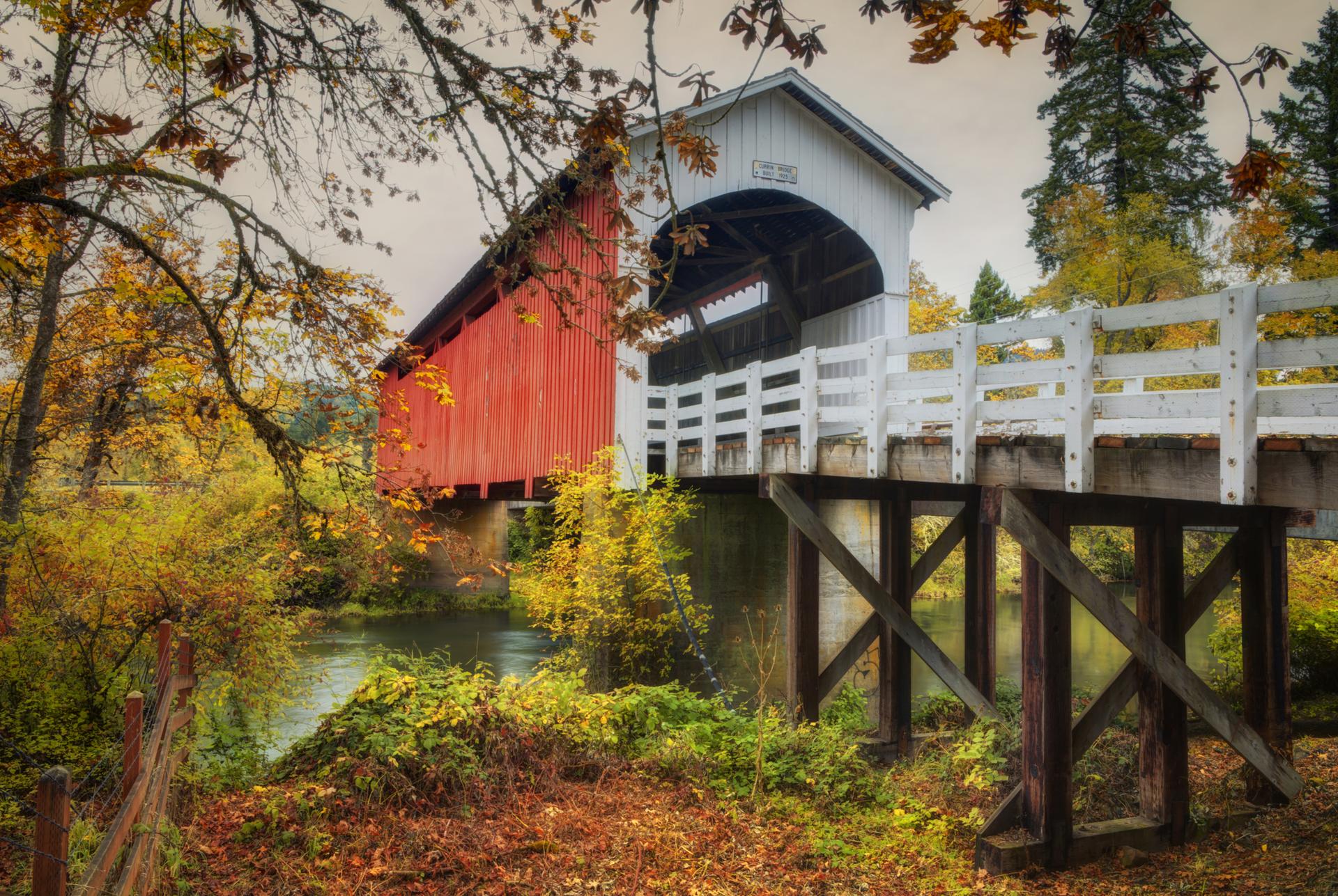 Red and white covered bridge over a river, surrounded by autumn foliage.