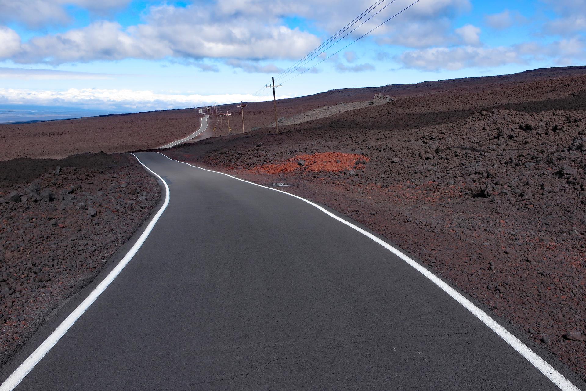 Winding road through a barren volcanic landscape under a partly cloudy sky.