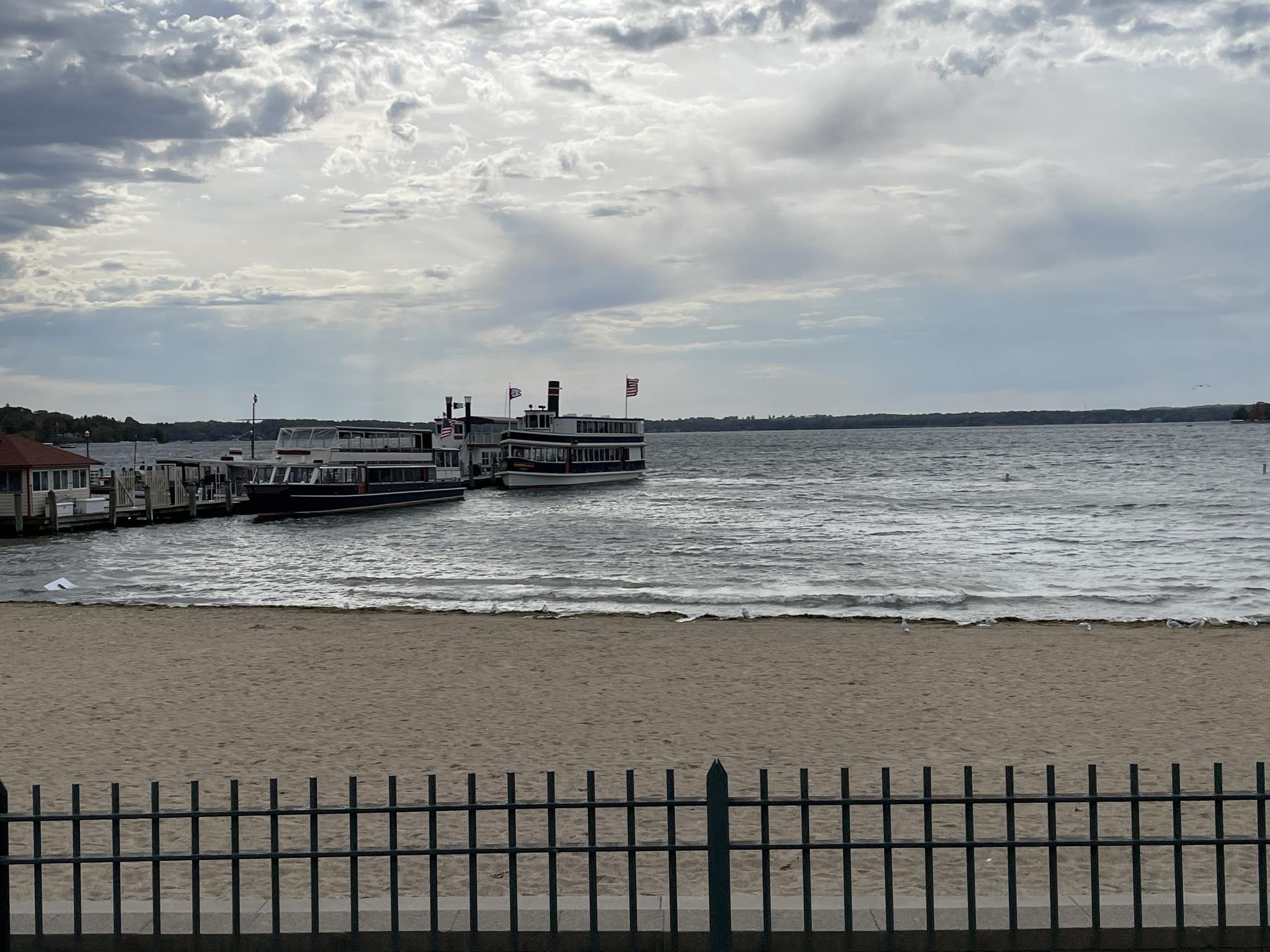 Two large passenger boats docked by a sandy beach on a wide lake.