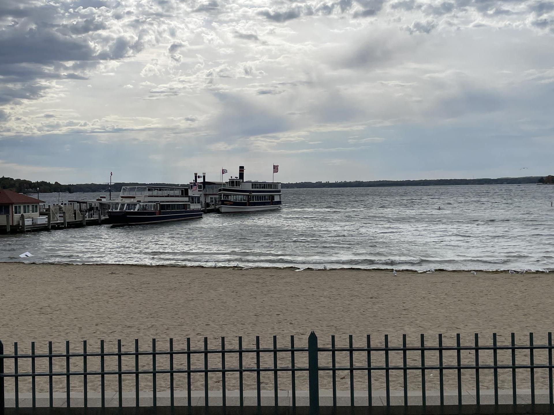 Two large passenger boats docked by a sandy beach on a wide lake.