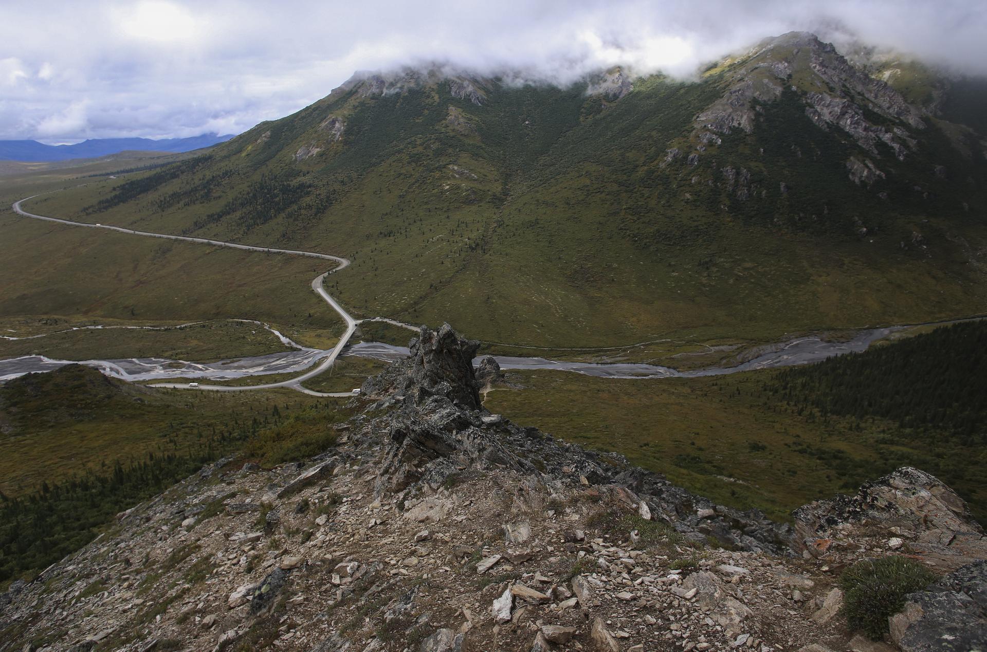 Rocky peak overlooking a valley with a winding road and river.
