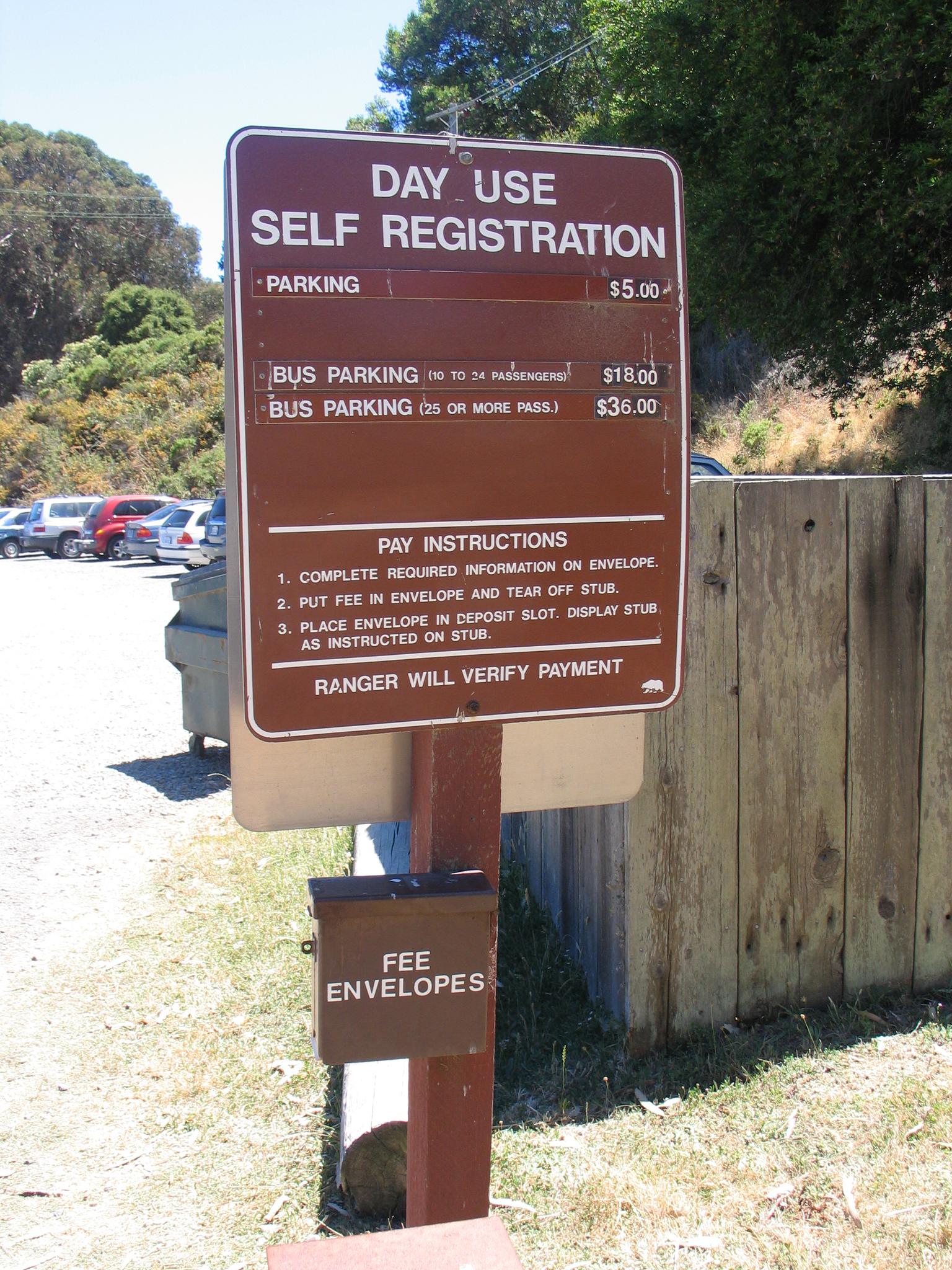 Brown 'Day Use Self Registration' sign with parking instructions in daylight.