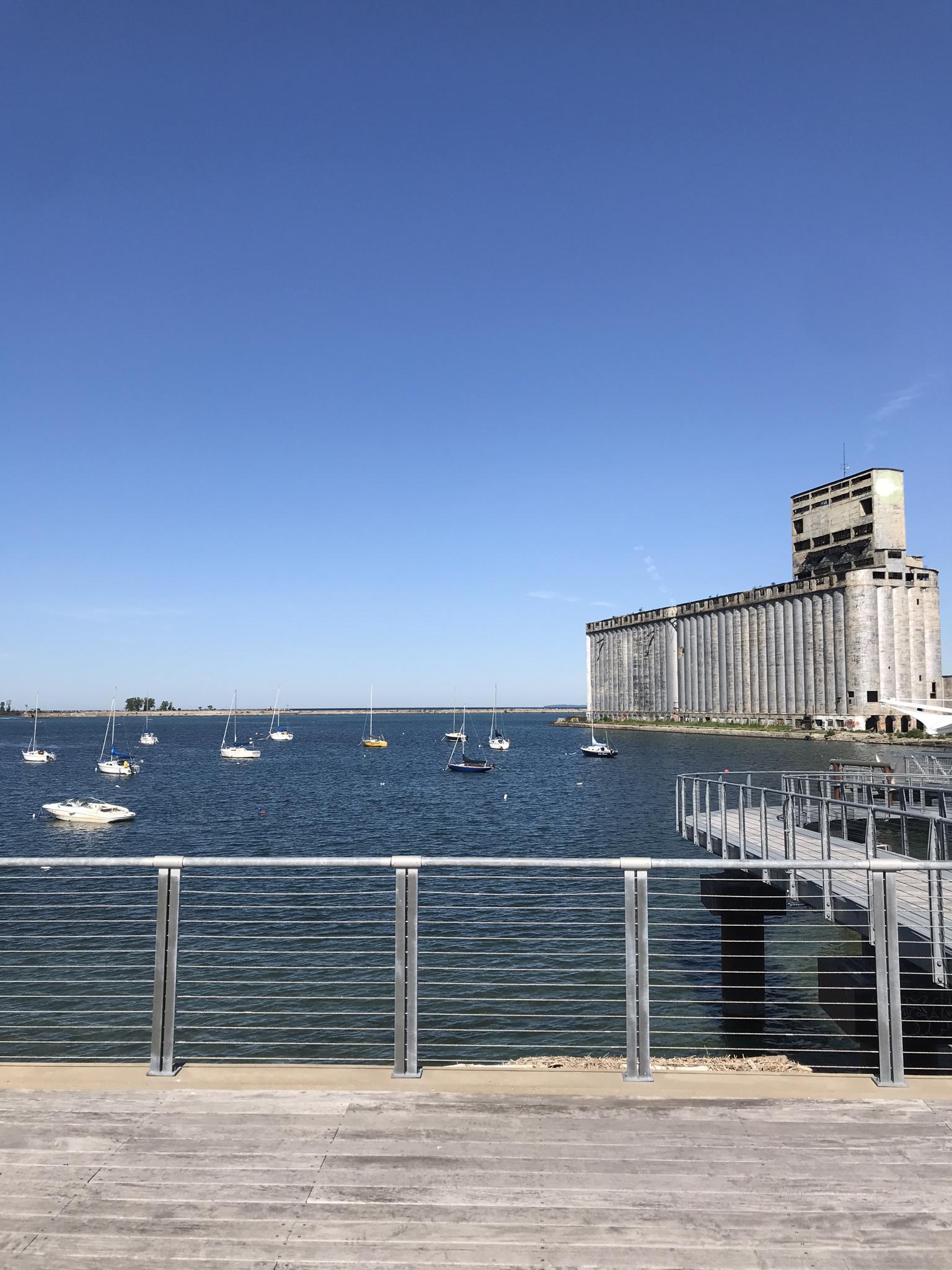 Large industrial building by water with boats and a wooden pier.