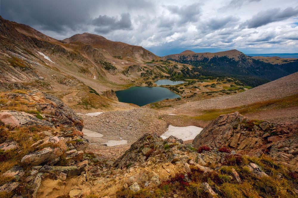 Rugged mountain landscape with two dark alpine lakes under a cloudy sky.