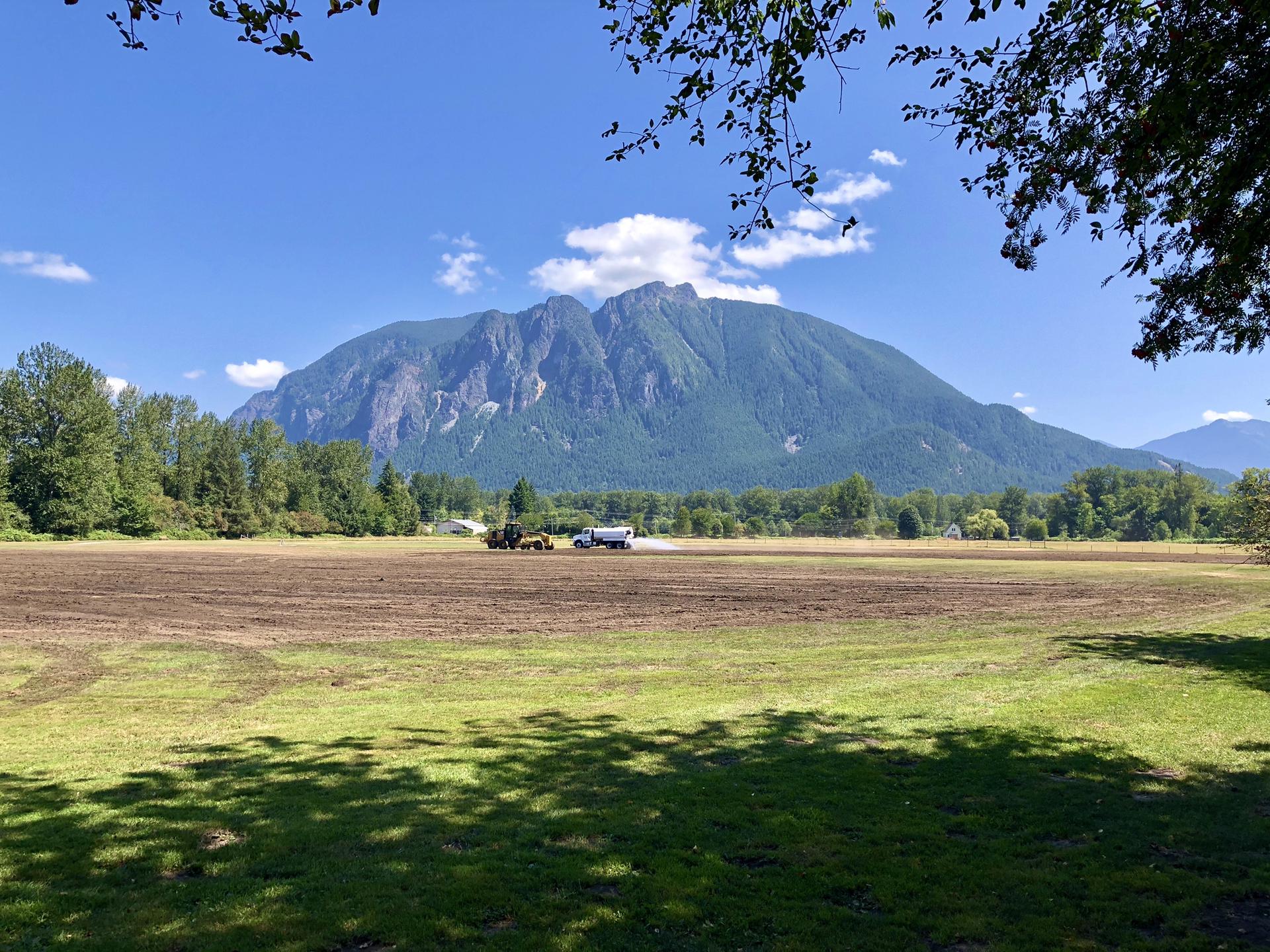 Bright day with a large mountain overlooking a green and brown field.