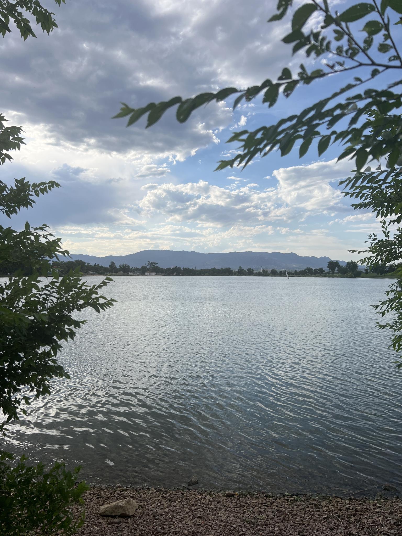 A calm lake with distant mountains under a cloudy sky, framed by leaves.