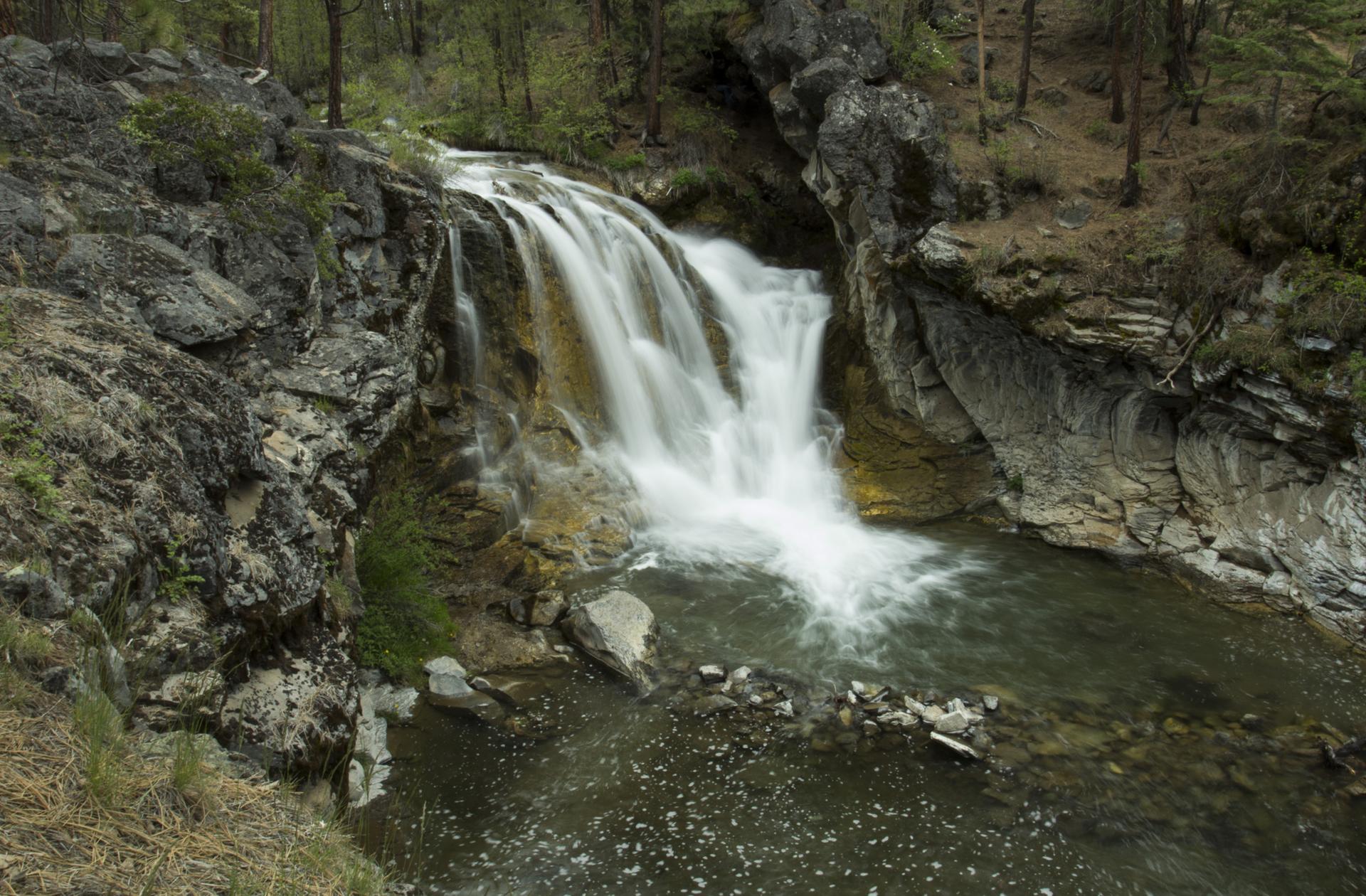 A powerful waterfall cascades into a rocky river in a lush forest.