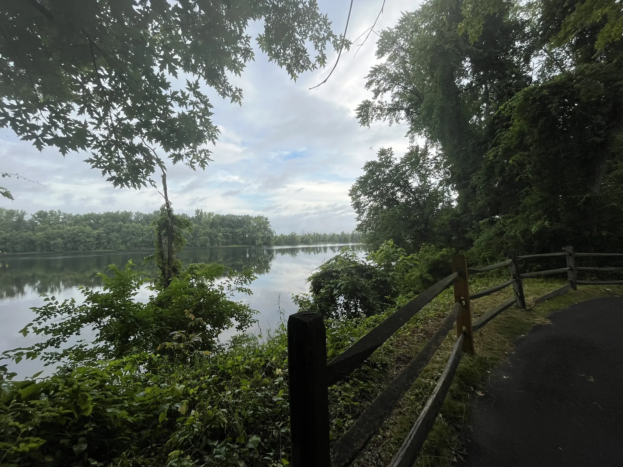 Calm river bordered by dense green trees and a rustic wooden fence. - Heritage Way Bikepath Loop
