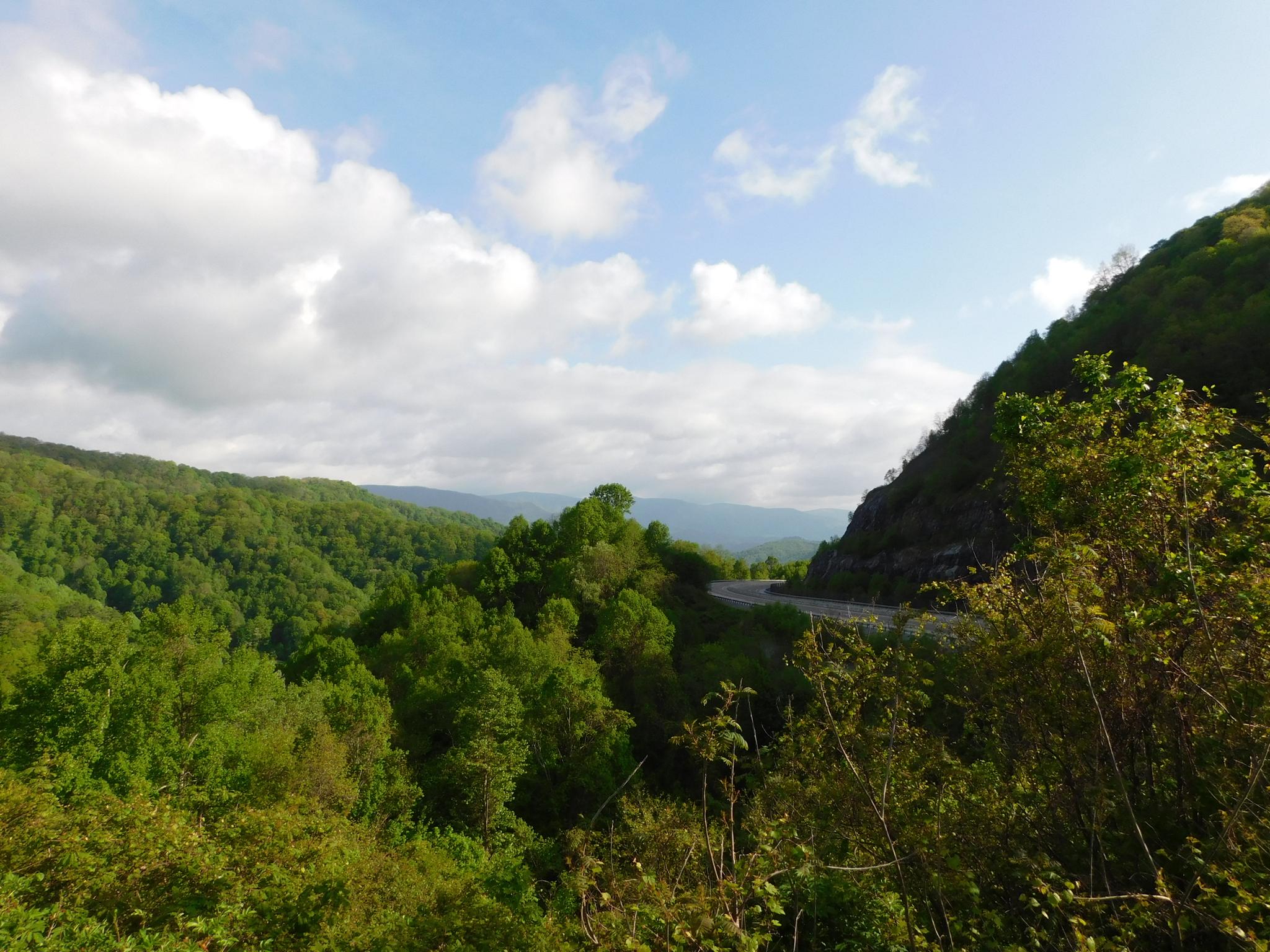 Lush green mountains and a winding road under a partly cloudy sky.