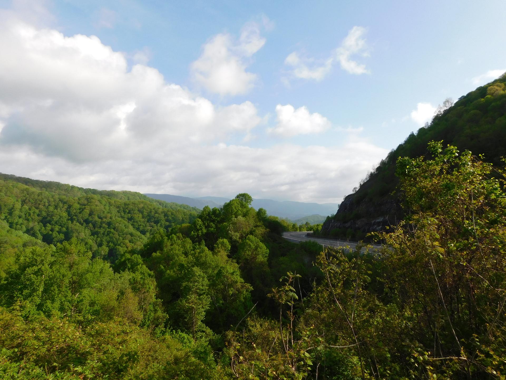 Lush green mountains and a winding road under a partly cloudy sky.