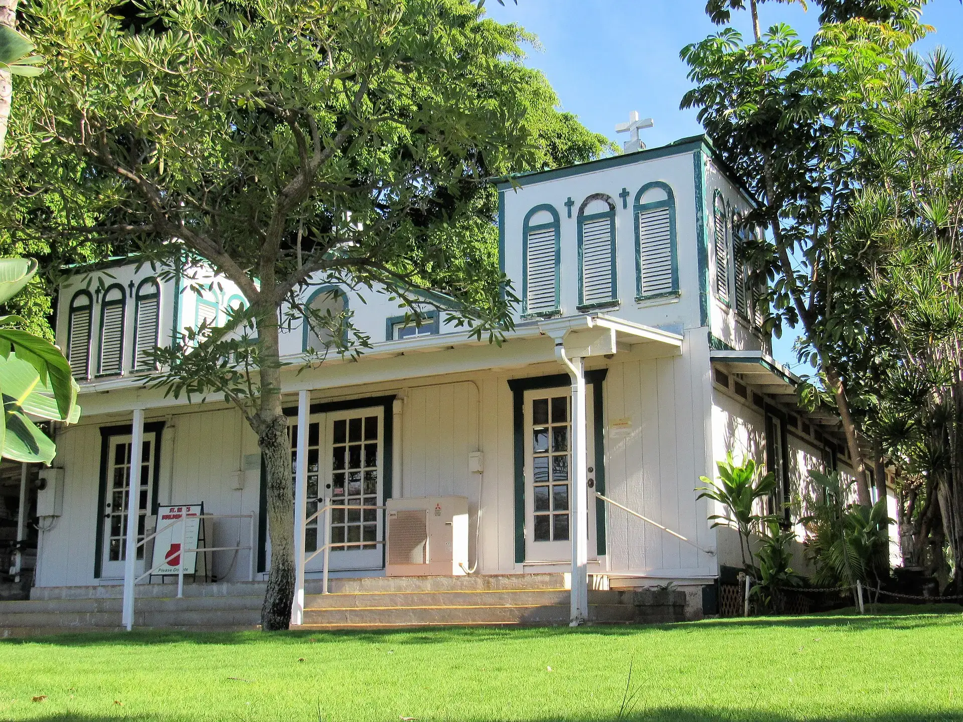 White building with green trim surrounded by lush trees on a sunny day.