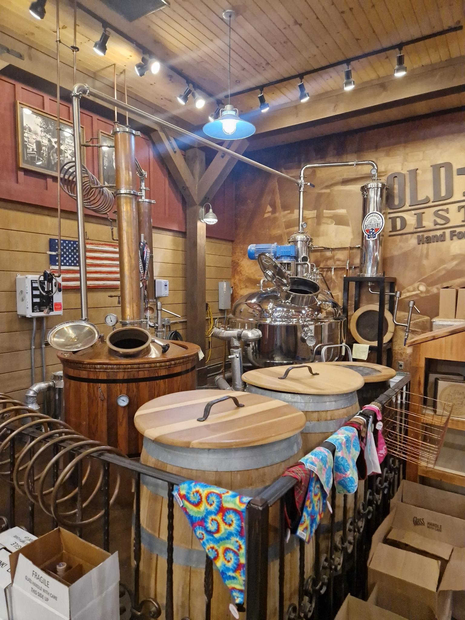 Indoor view of distillery equipment with large stills and wooden barrels.