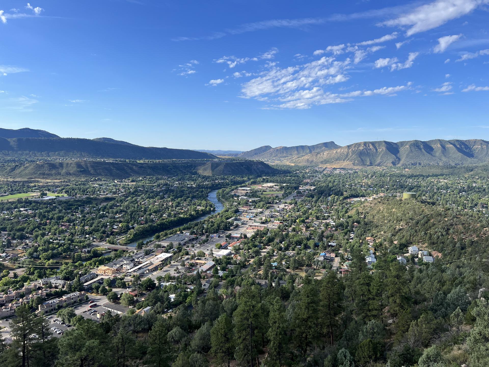 Aerial view of a town and river in a green valley, surrounded by mountains.