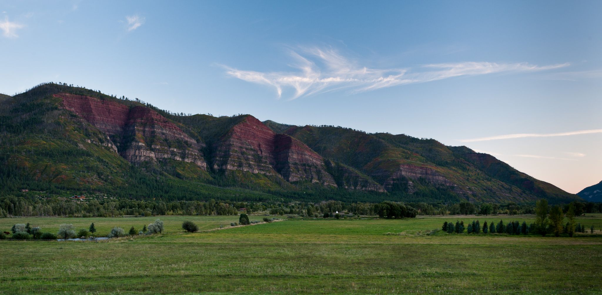 Expansive green fields before layered mountains under a clear blue sky. - Hermosa Valley via CR 250 & CR 203 loop
