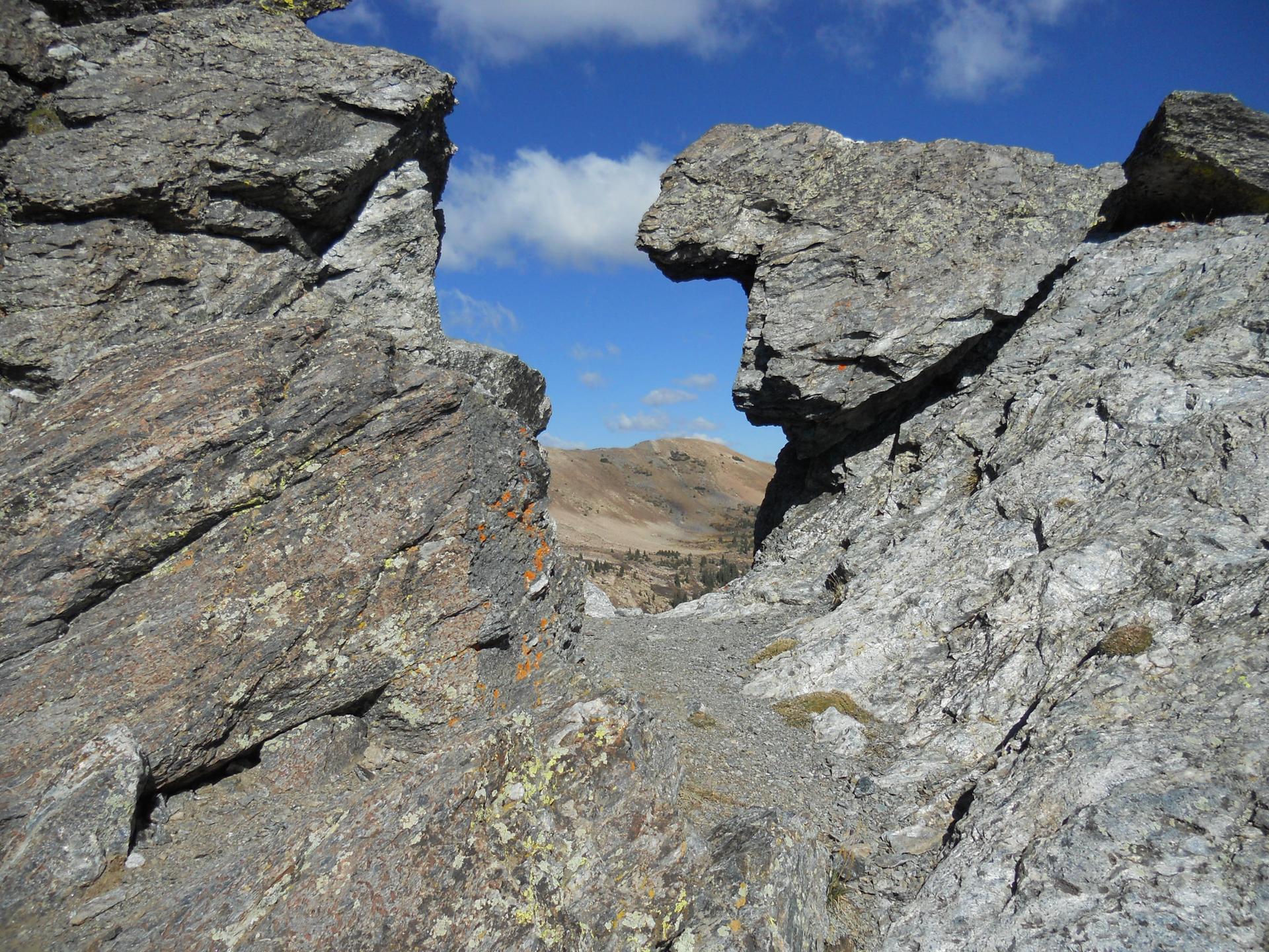 Sunlit rocky outcrop frames a distant mountain under a blue sky.