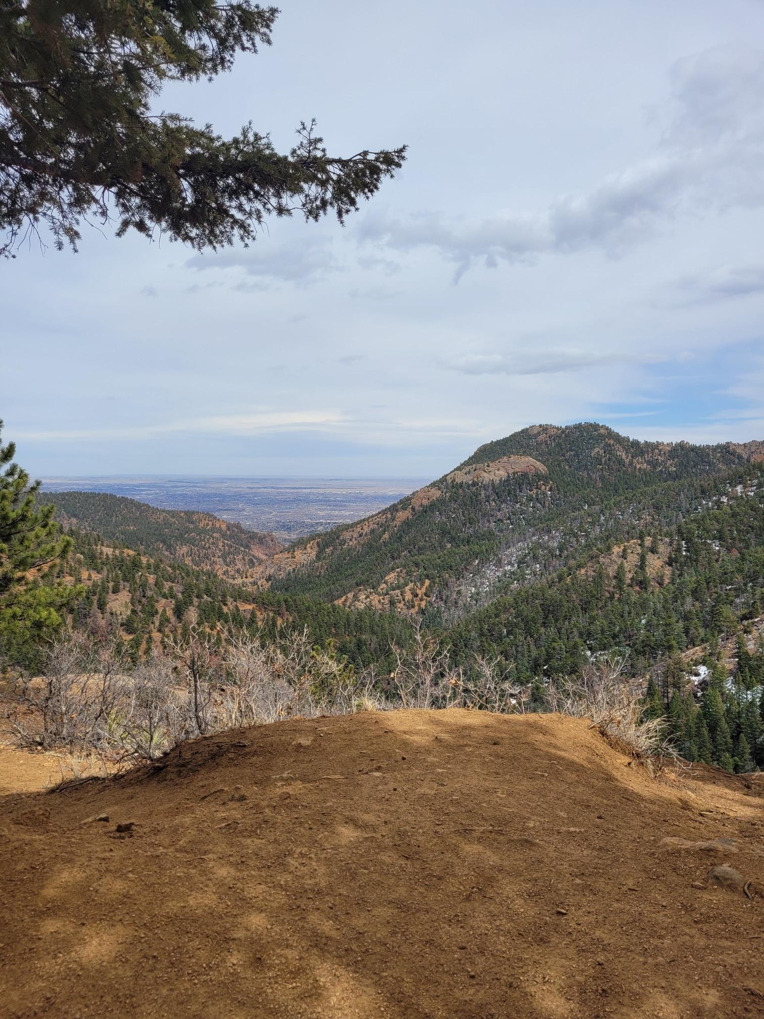 A wide view of pine-covered mountains and a distant valley under a cloudy sky.