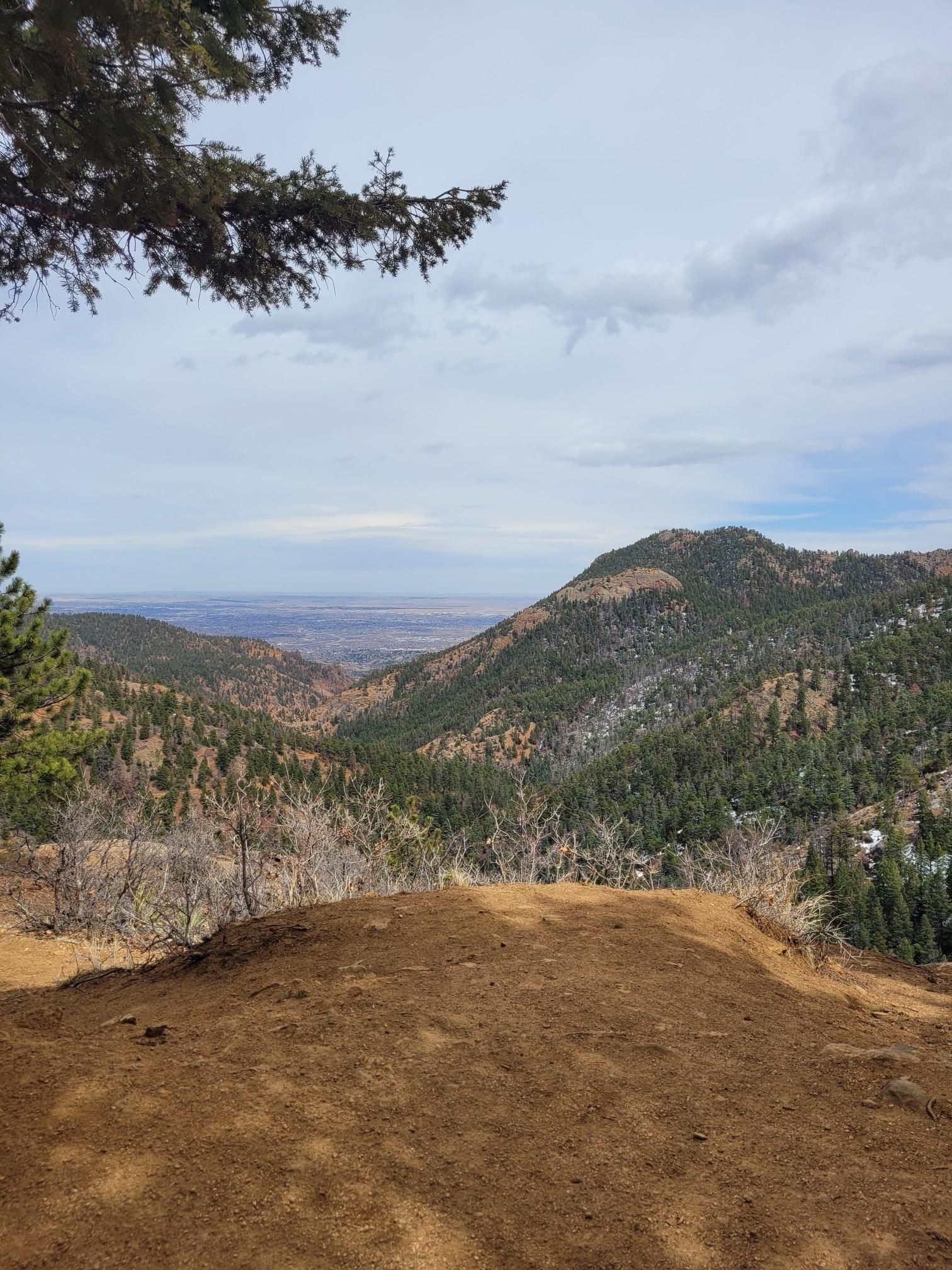 A wide view of pine-covered mountains and a distant valley under a cloudy sky. - Cripple Creek from Colorado Springs on the Gold Camp Road