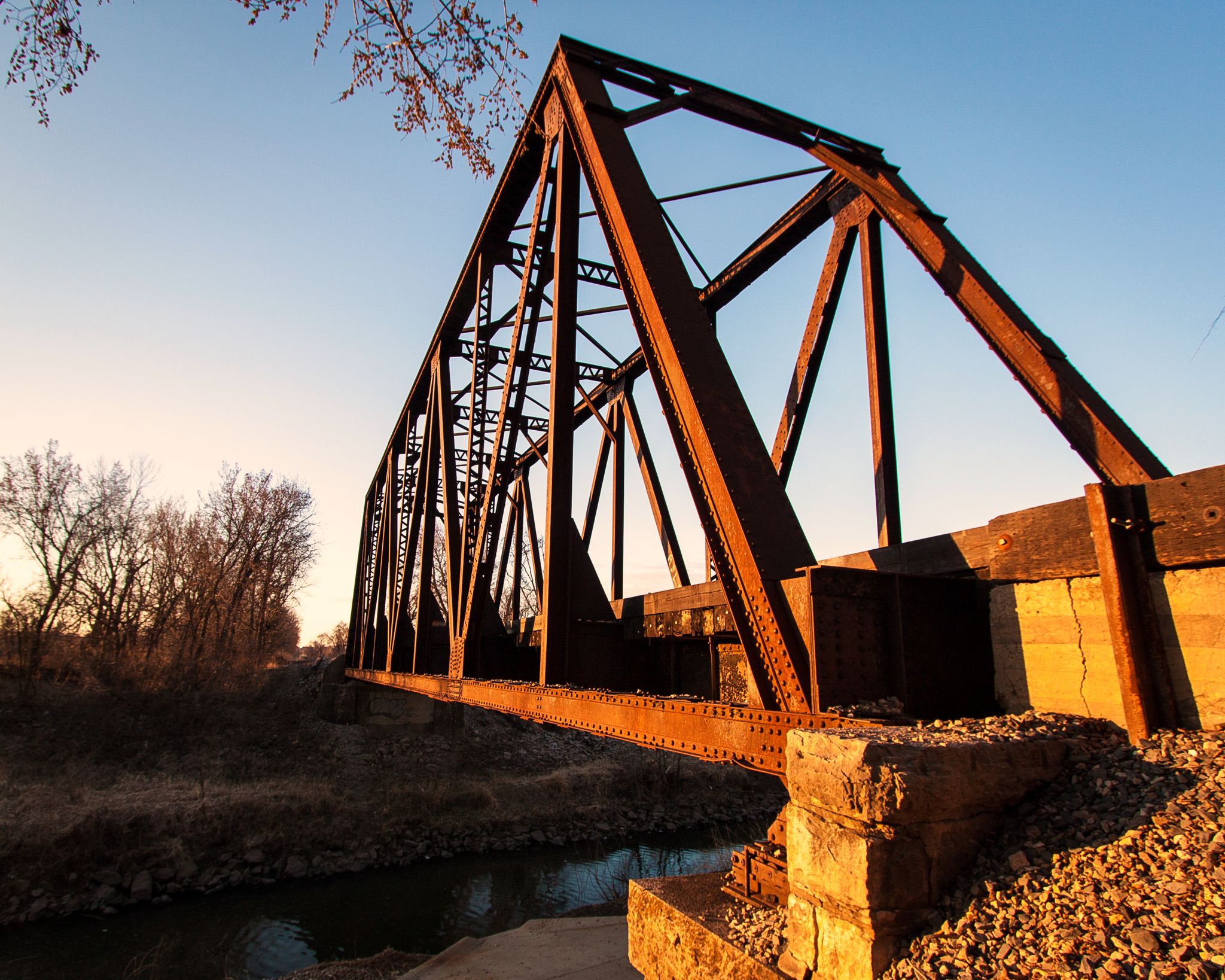 A rusty metal truss bridge spans a river at golden hour. - Little Blue Trace Trail – Little Blue Trail Park loop from Country Meadows South