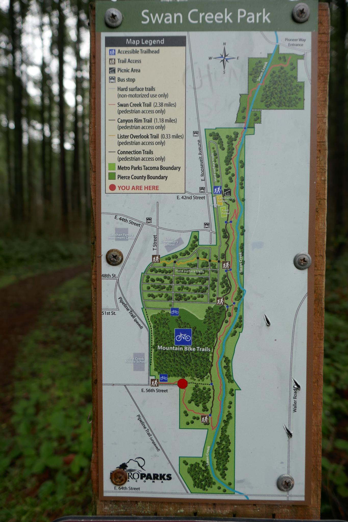 A detailed park map displayed on a wooden sign in a forest.