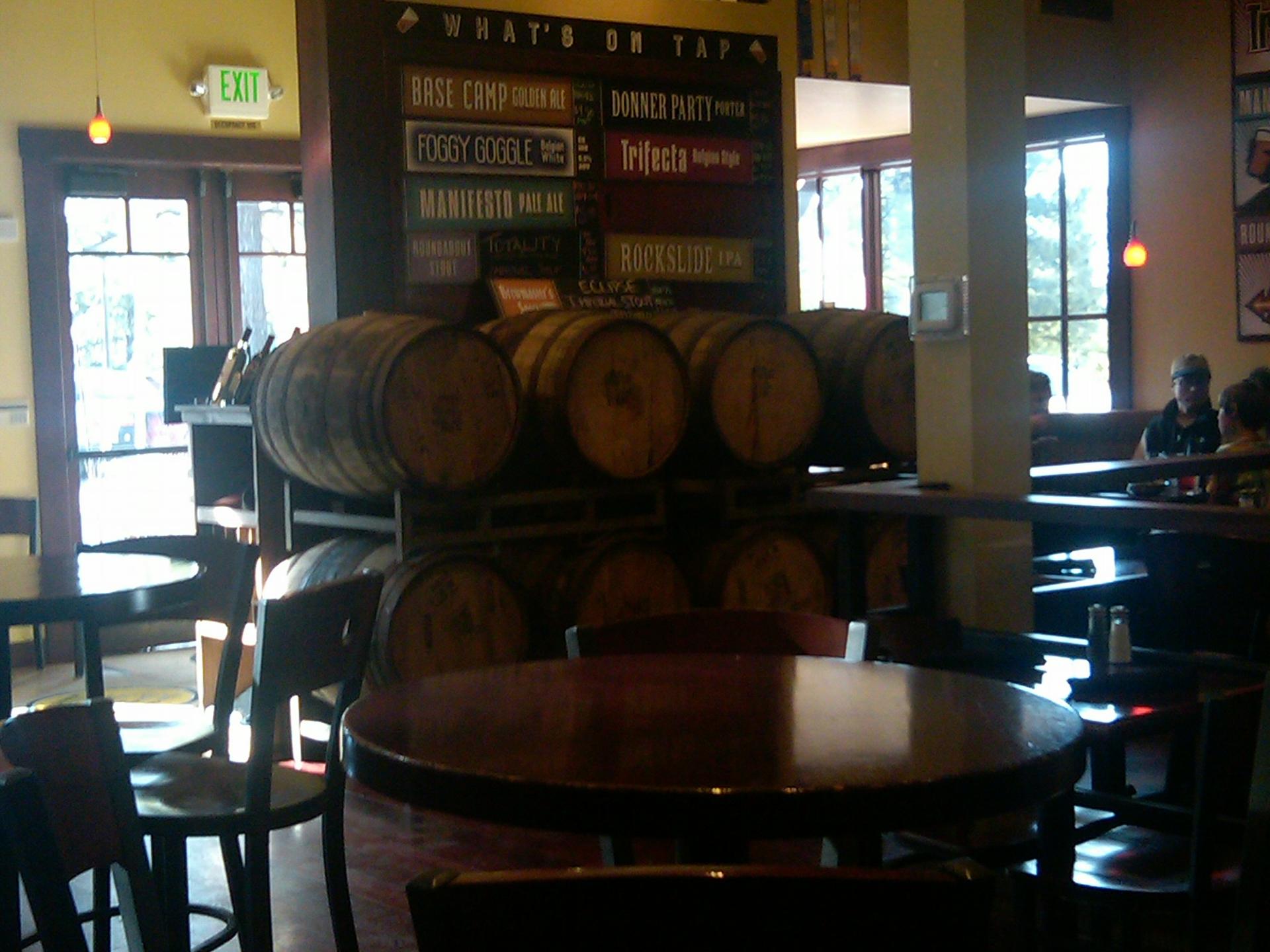 Interior of a pub with wooden barrels, tables, and people in the background.