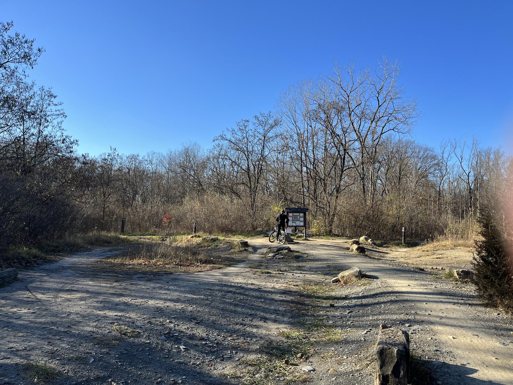 Person on a bicycle at a dirt path intersection under a clear blue sky. - East Rim mountain bike trails – East Rim MTB Trailhead loop from Chittendens Corners